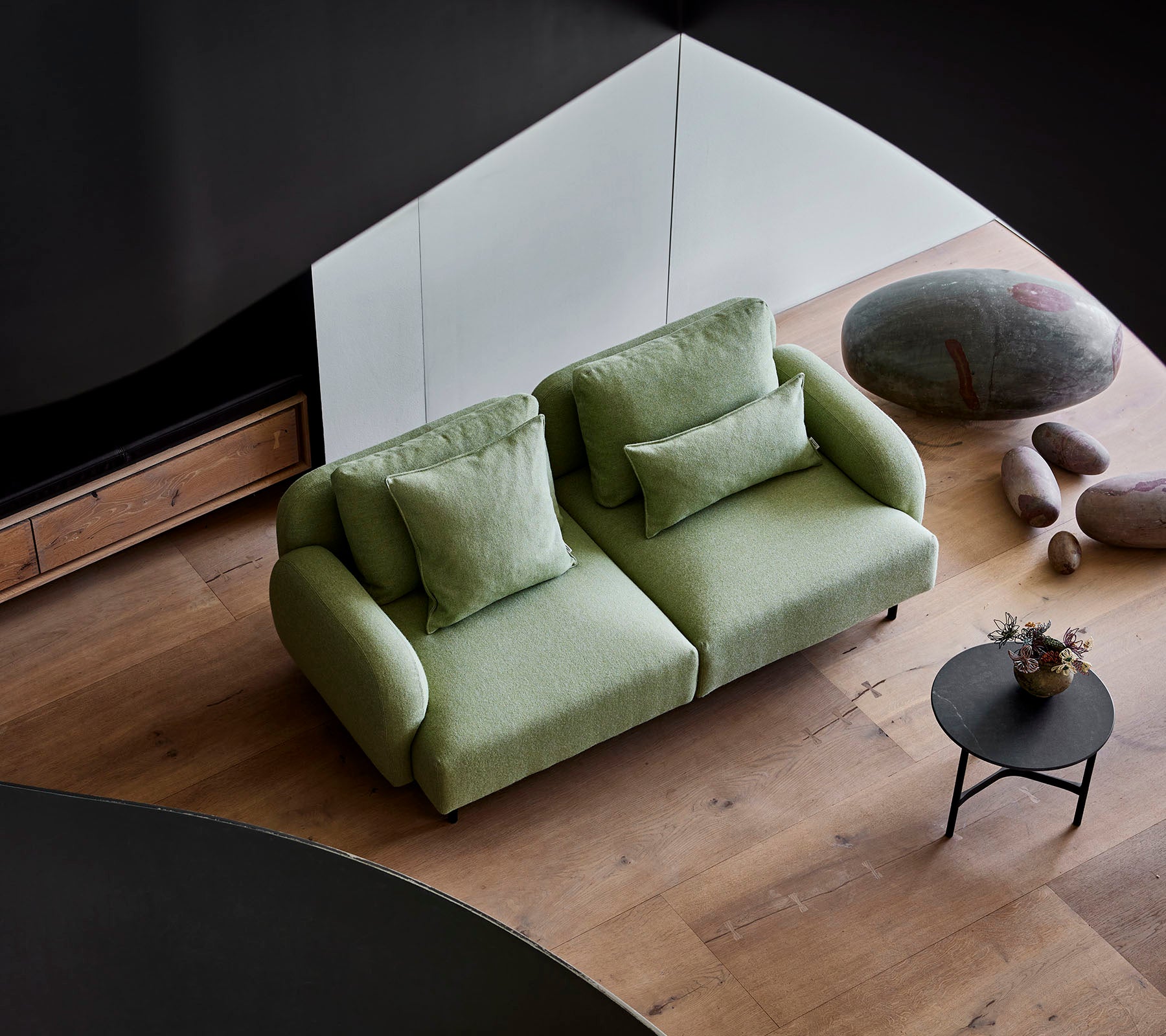 Stijlvolle groene bank met pluche kussens naast een kleine ronde tafel, tegen een moderne achtergrond met houten vloeren en gladde stenen.