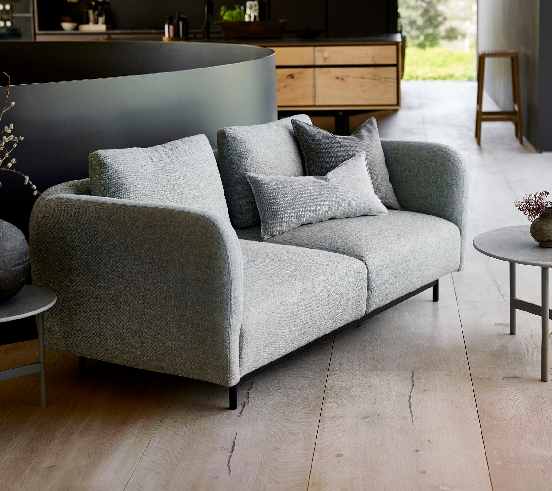 Moderne grijze bank met pluche kussens, gecombineerd met een kleine ronde tafel, tegen een minimalistisch achtergrond.