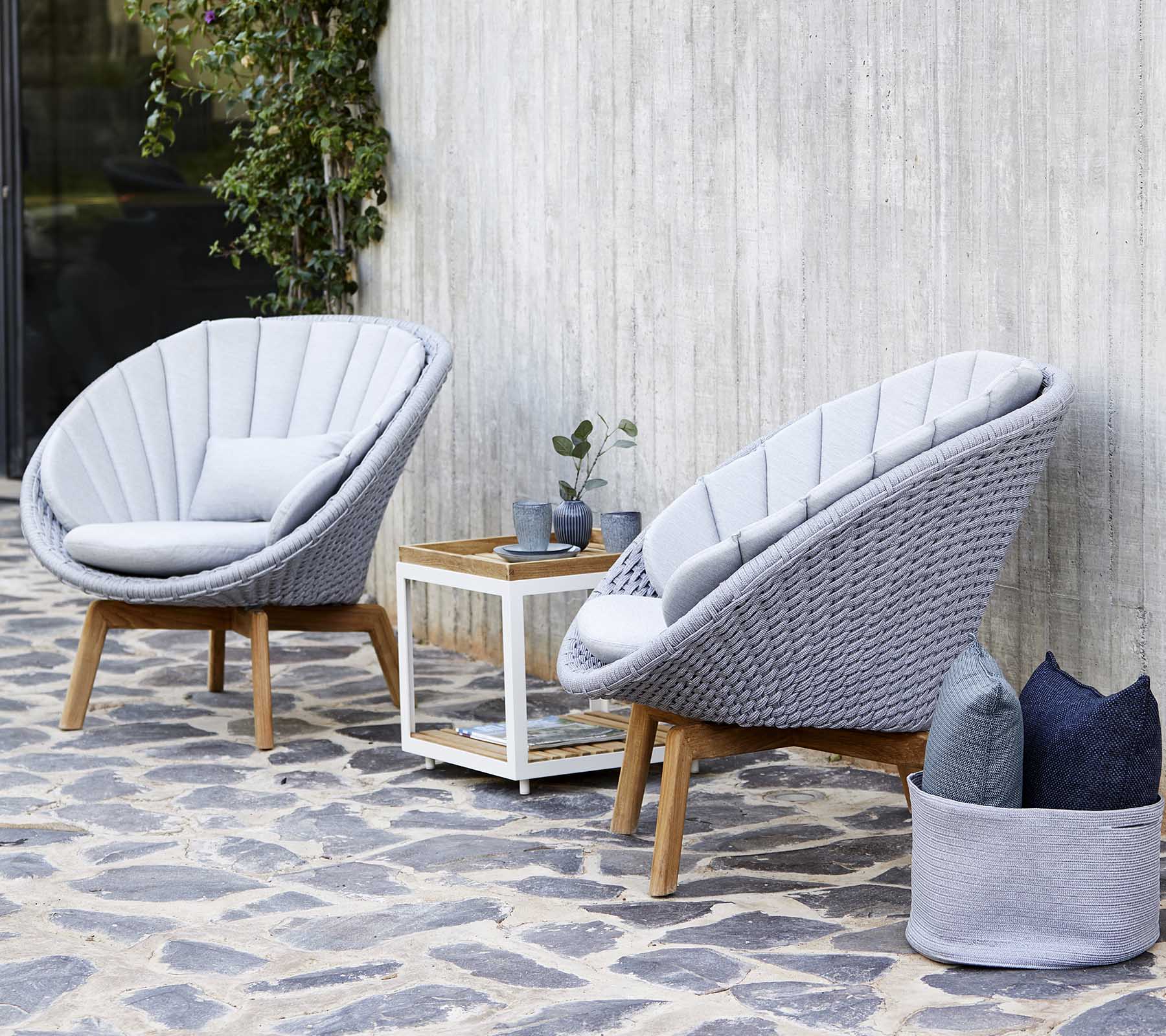 Twee stijlvolle grijze loungestoelen met een houten frame staan naast een witte salontafel, versierd met een kleine plant en decoratieve kussens.