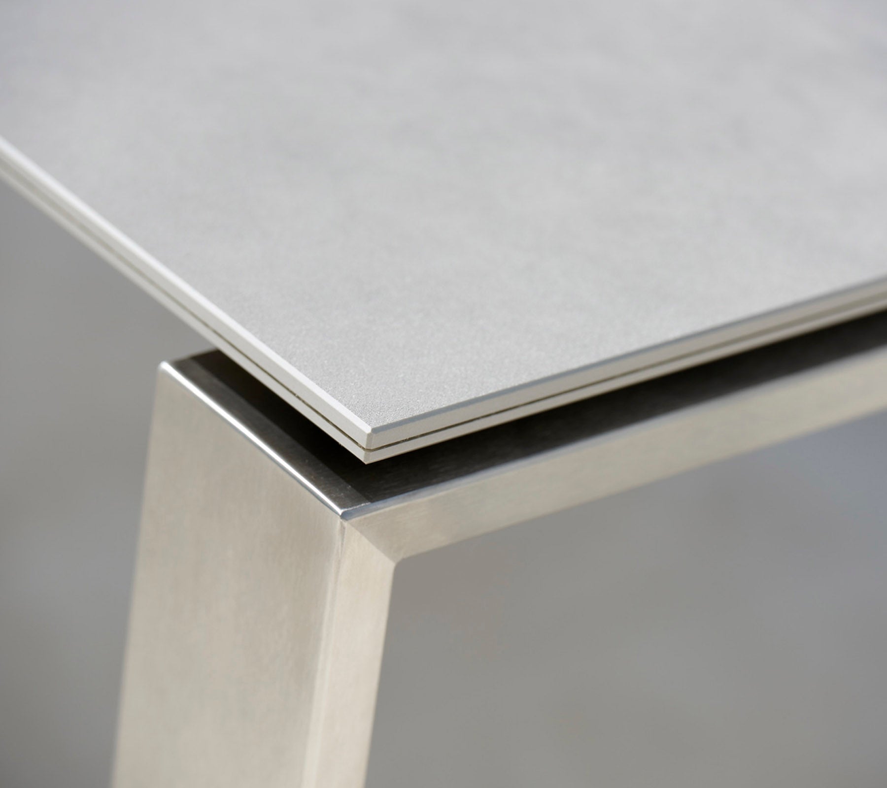 Close-up van een moderne tafel met een slanke grijze top en een roestvrijstalen basis, die de contrasterende materialen en strakke lijnen benadrukt.