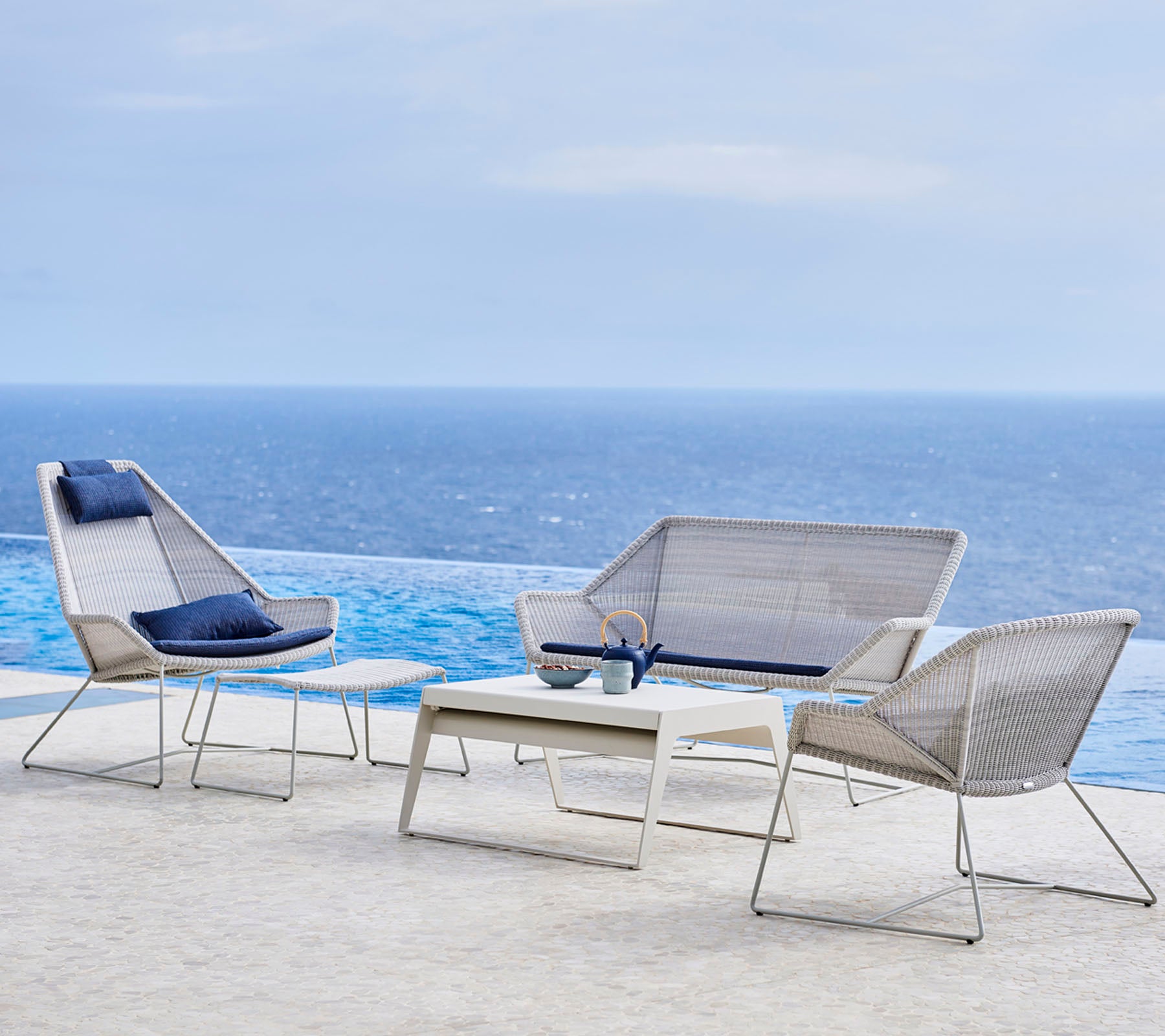 Modern tuinmeubelset met stijlvolle stoelen en een tafel, tegen een achtergrond van water en lucht.
