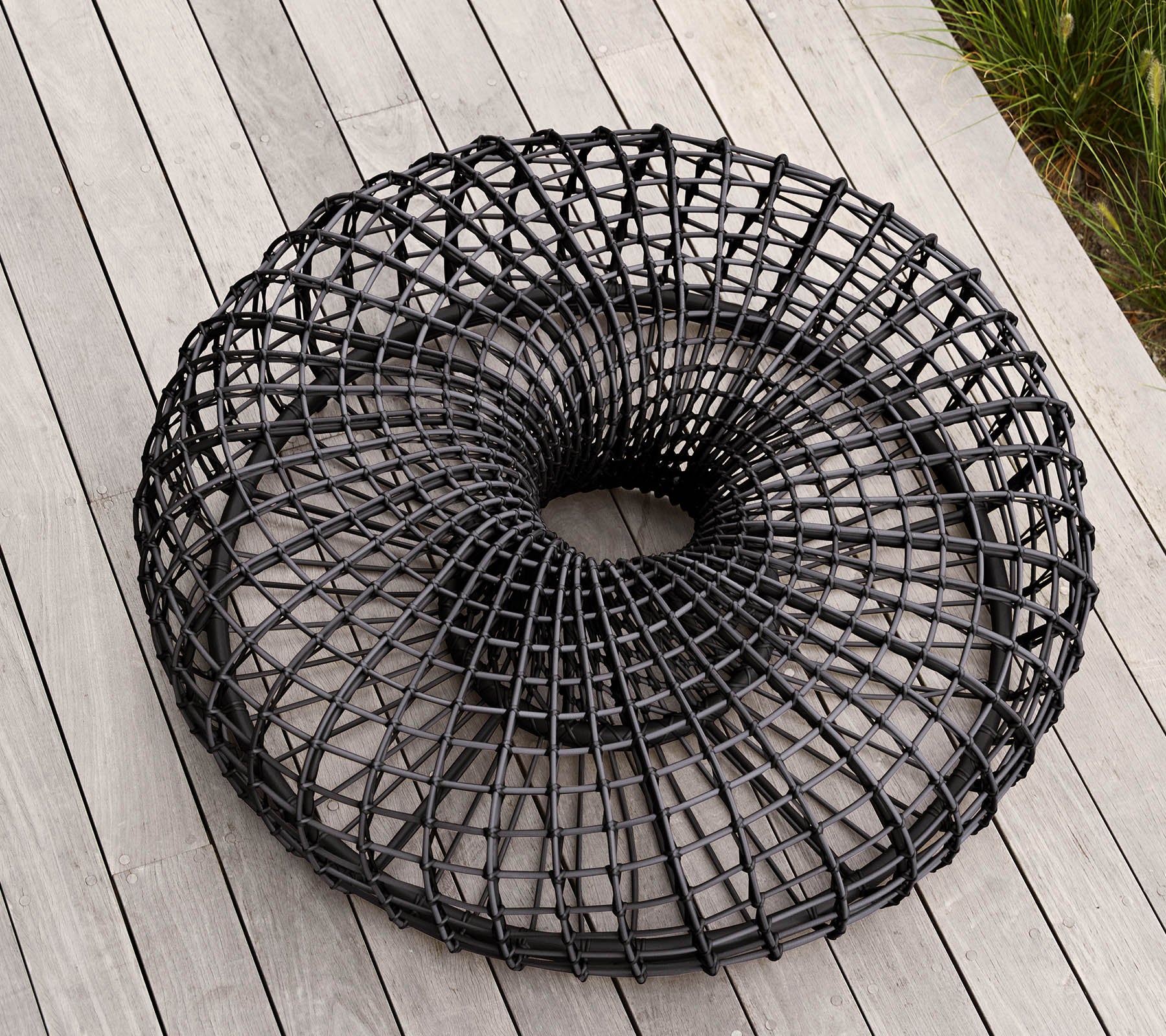 Moderne, ronde zwarte draadmand met een uniek open vlechtontwerp, die op een vlakke ondergrond rust. Ideaal voor opslag of decoratieve doeleinden.