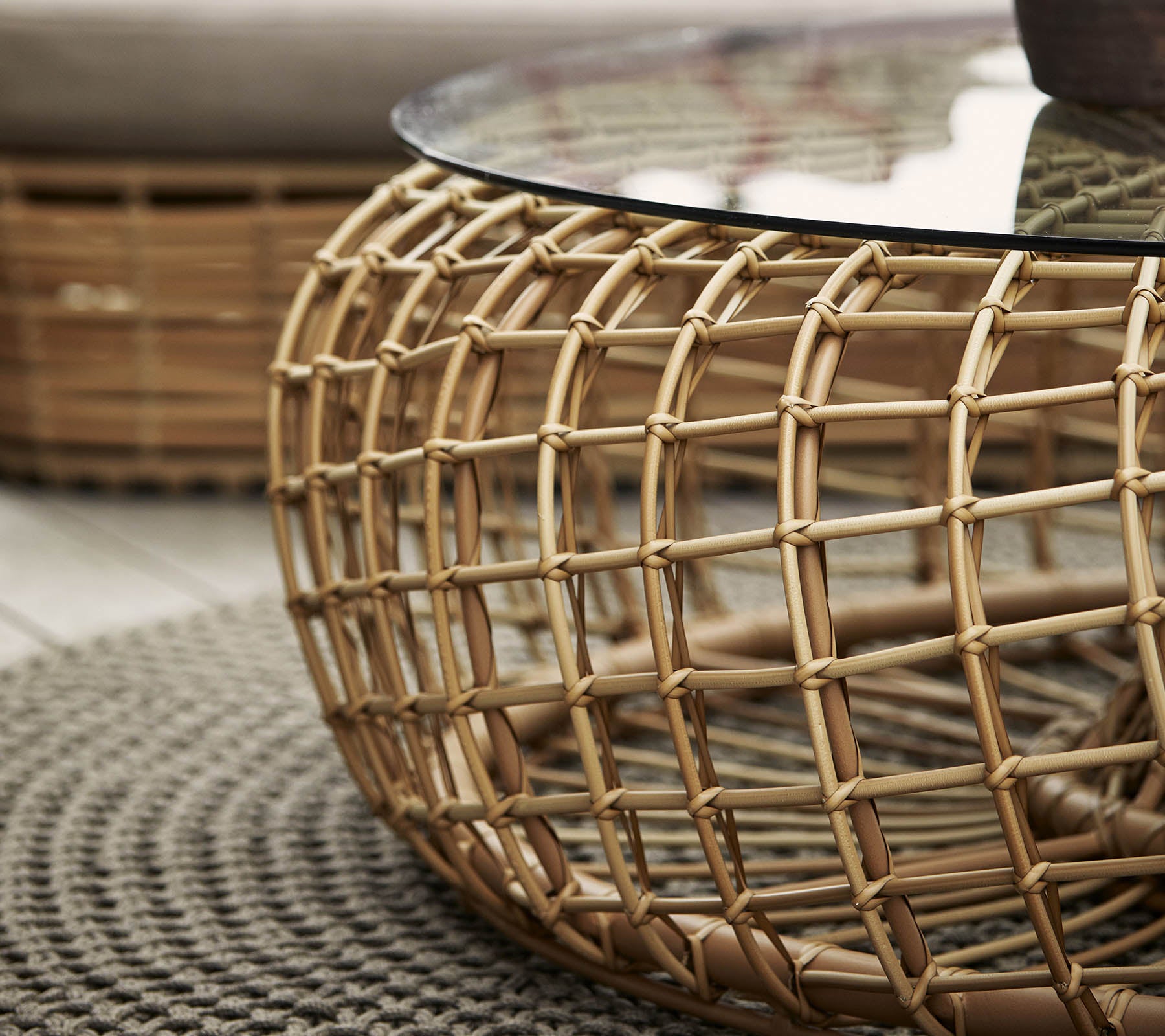 Rond koffie tafel met een geweven rattan basis en een glazen bovenblad, aangevuld met een textuur rond tapijt.