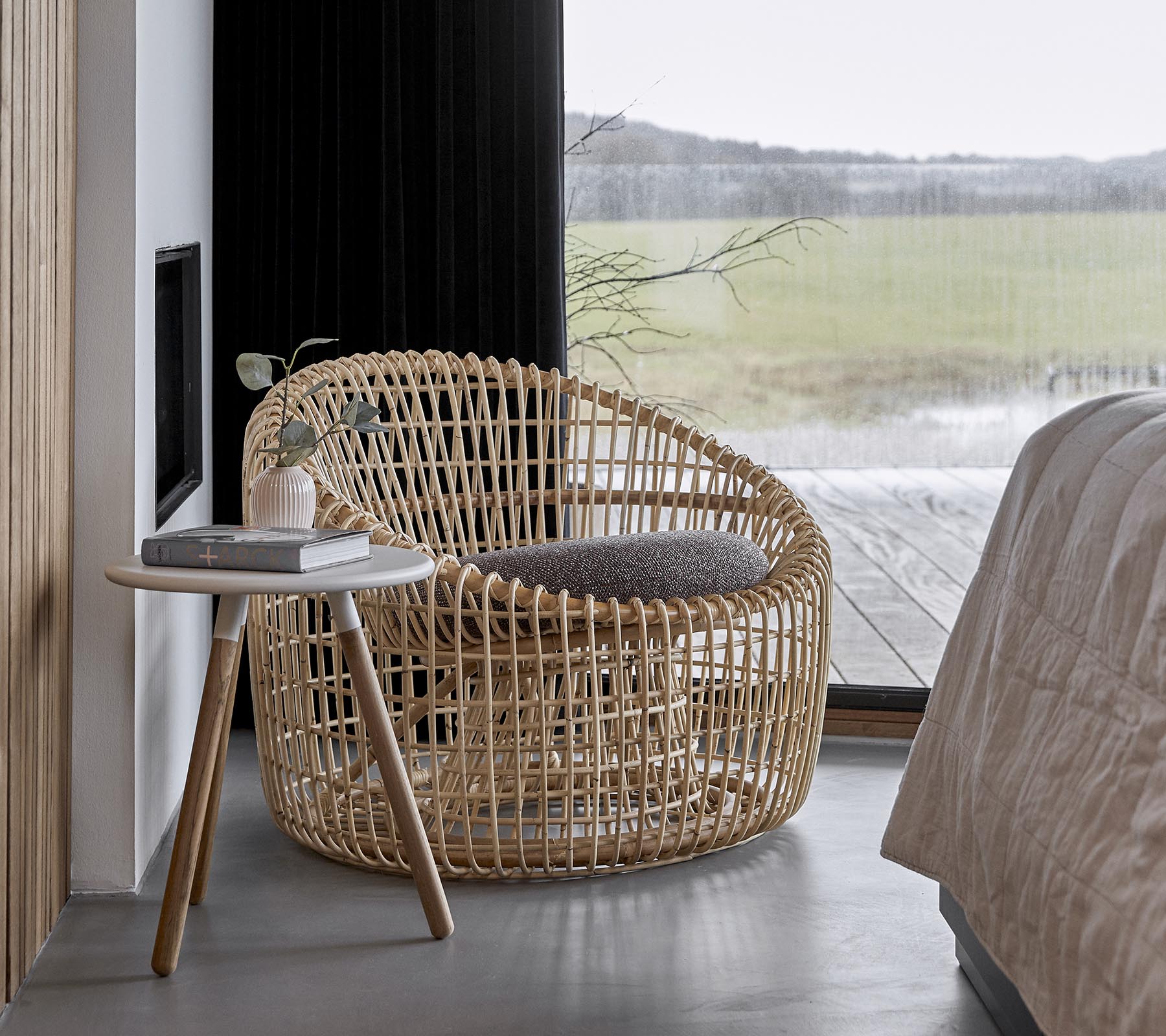 Een stijlvolle gevlochten stoel in combinatie met een klein bijzettafeltje, geplaatst in een serene omgeving met grote ramen die natuurlijk licht binnenlaten.
