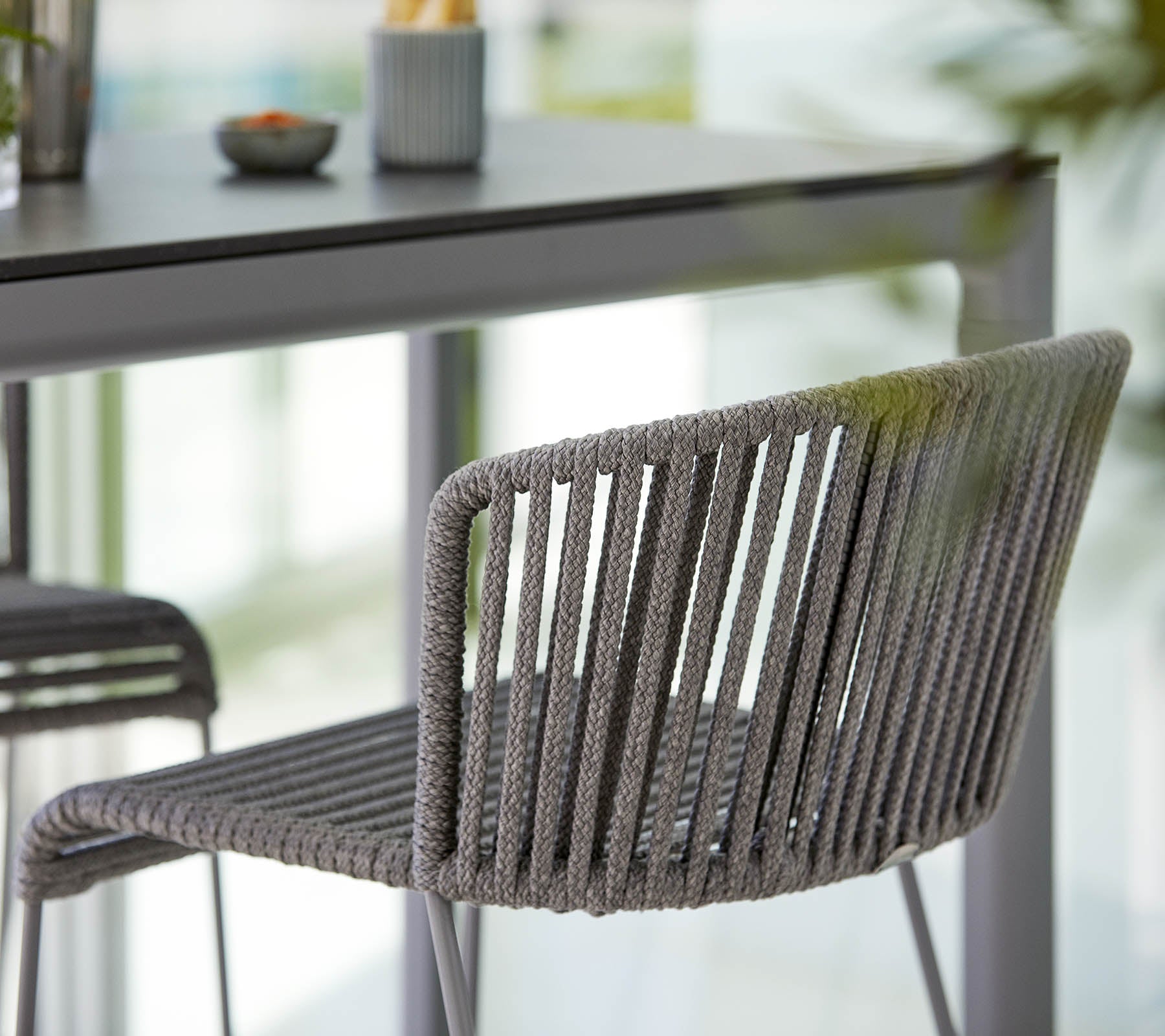 Stijlvolle grijze stoel met een slank ontwerp, met verticale strepen en een moderne esthetiek, geplaatst naast een minimalistische tafel.
