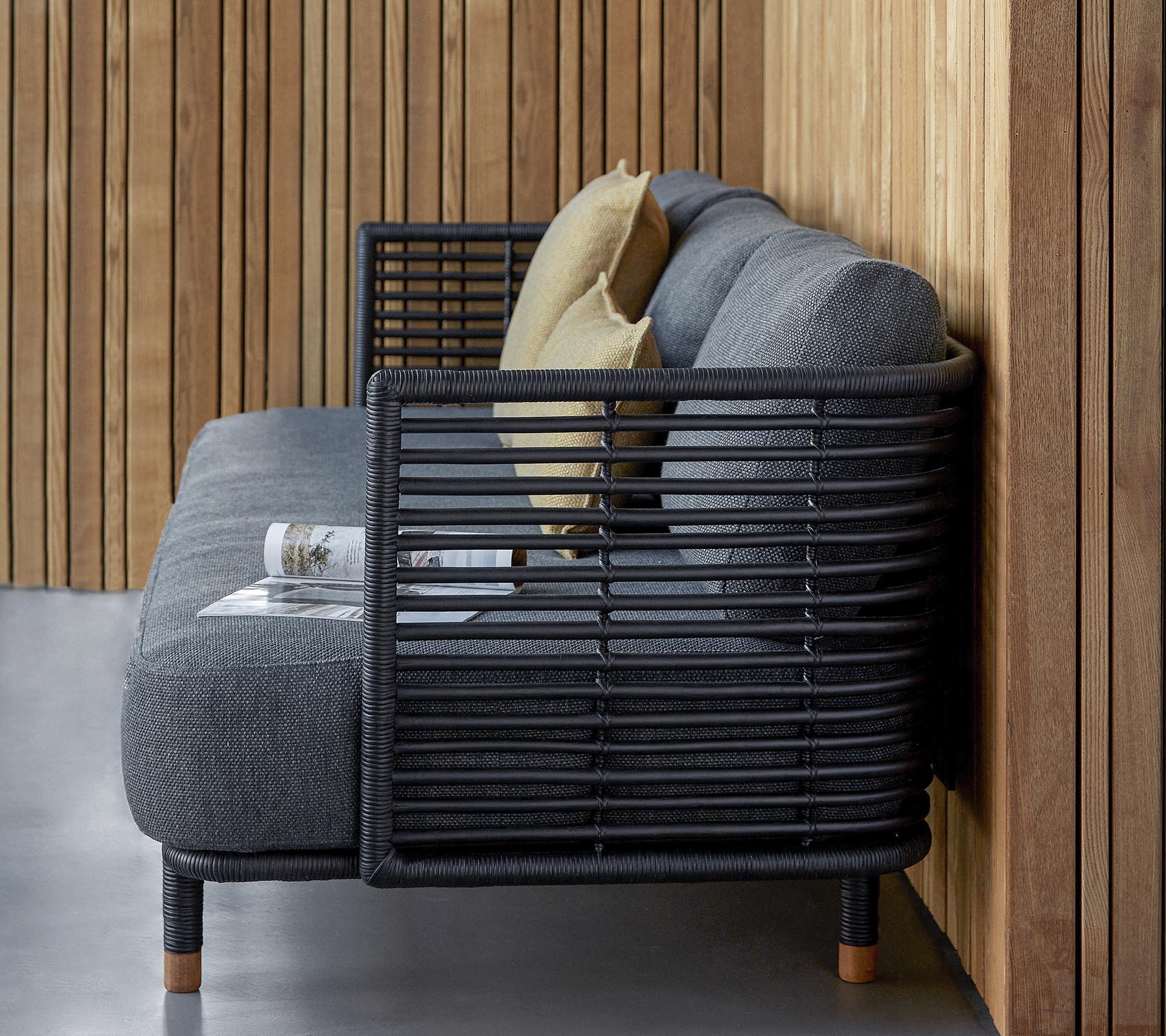 Stijlvolle bank met een slank ontwerp van gestructureerde grijze stof en decoratieve kussens, aangevuld met een modern lattenframe.