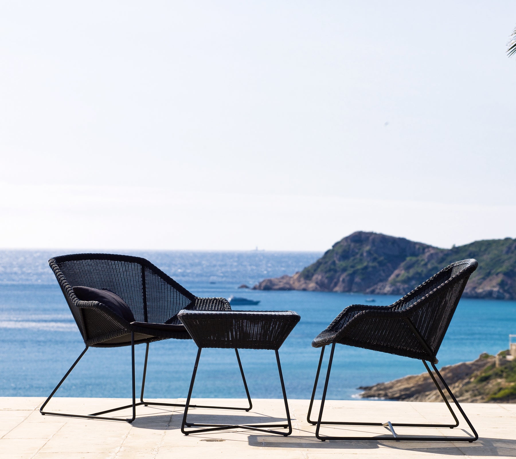 Twee zwarte stoelen en een zwart tafeltje met uitzicht op de kust.