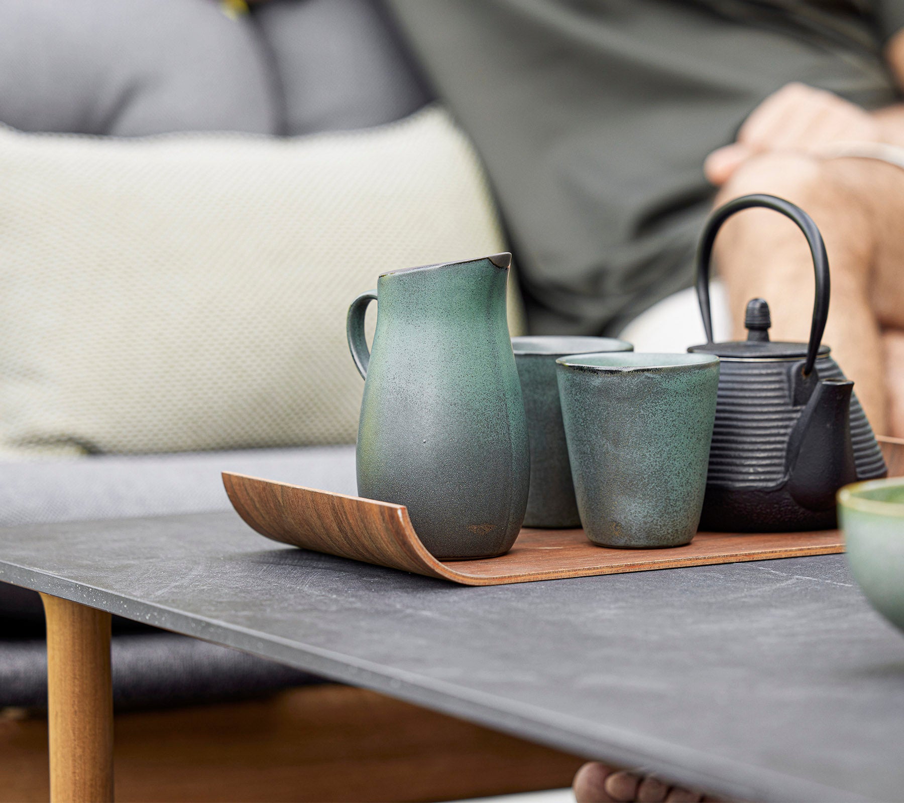Een stijlvolle schikking van keramische theepot, kopjes en een kan op een houten dienblad, dat modern design en aardetonen laat zien.