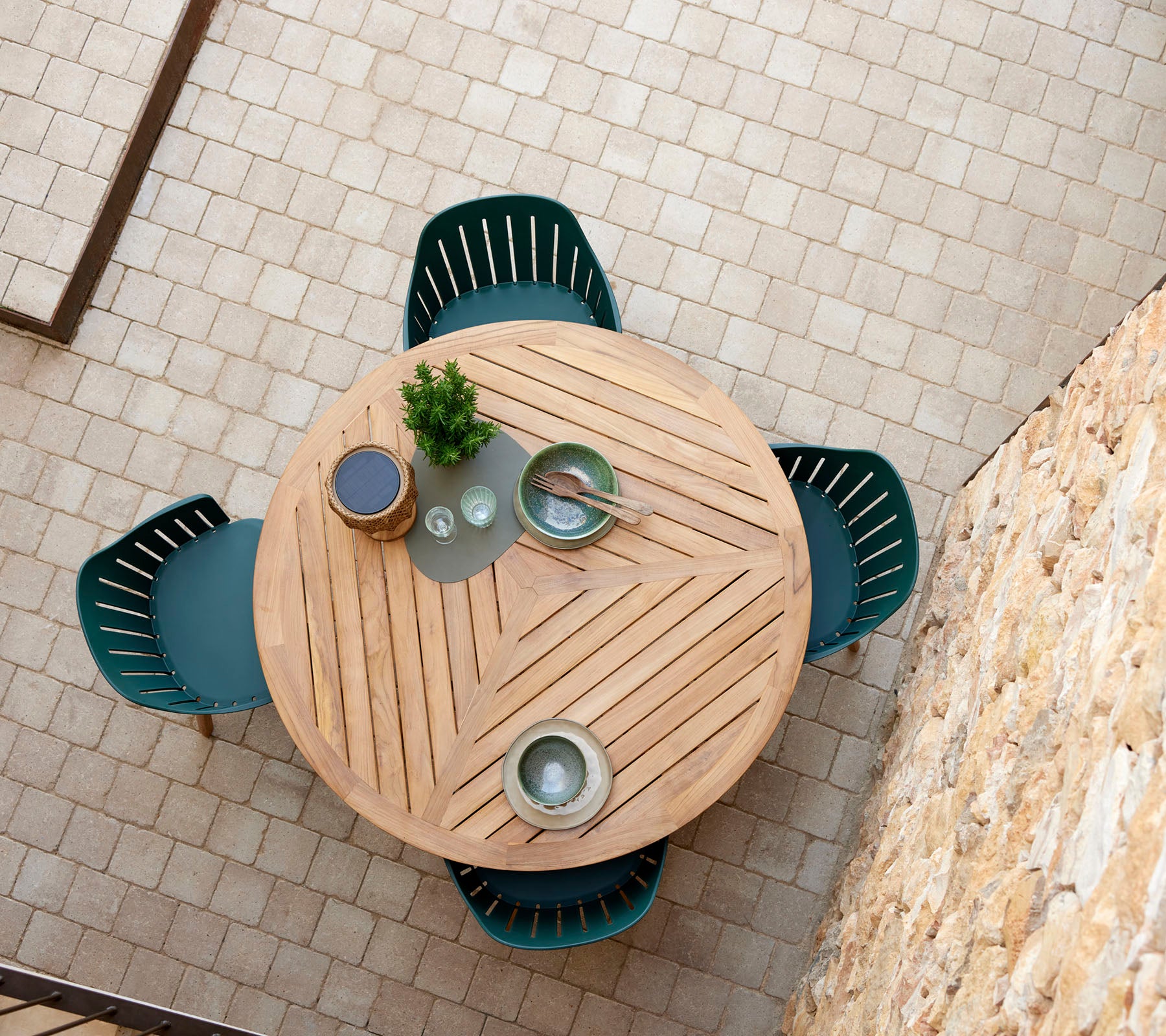 Een ronde houten tafel met een chevronpatroon, omringd door vier groene stoelen, en versierd met decoratieve borden en een kleine plant.