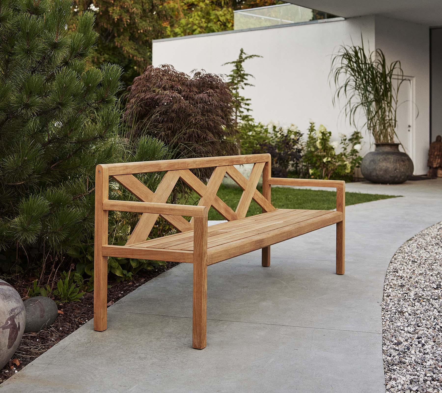 Een stijlvolle houten bank met een decoratieve rugleuning, omgeven door groen en decoratieve elementen, perfect voor ontspanning in de buitenlucht.