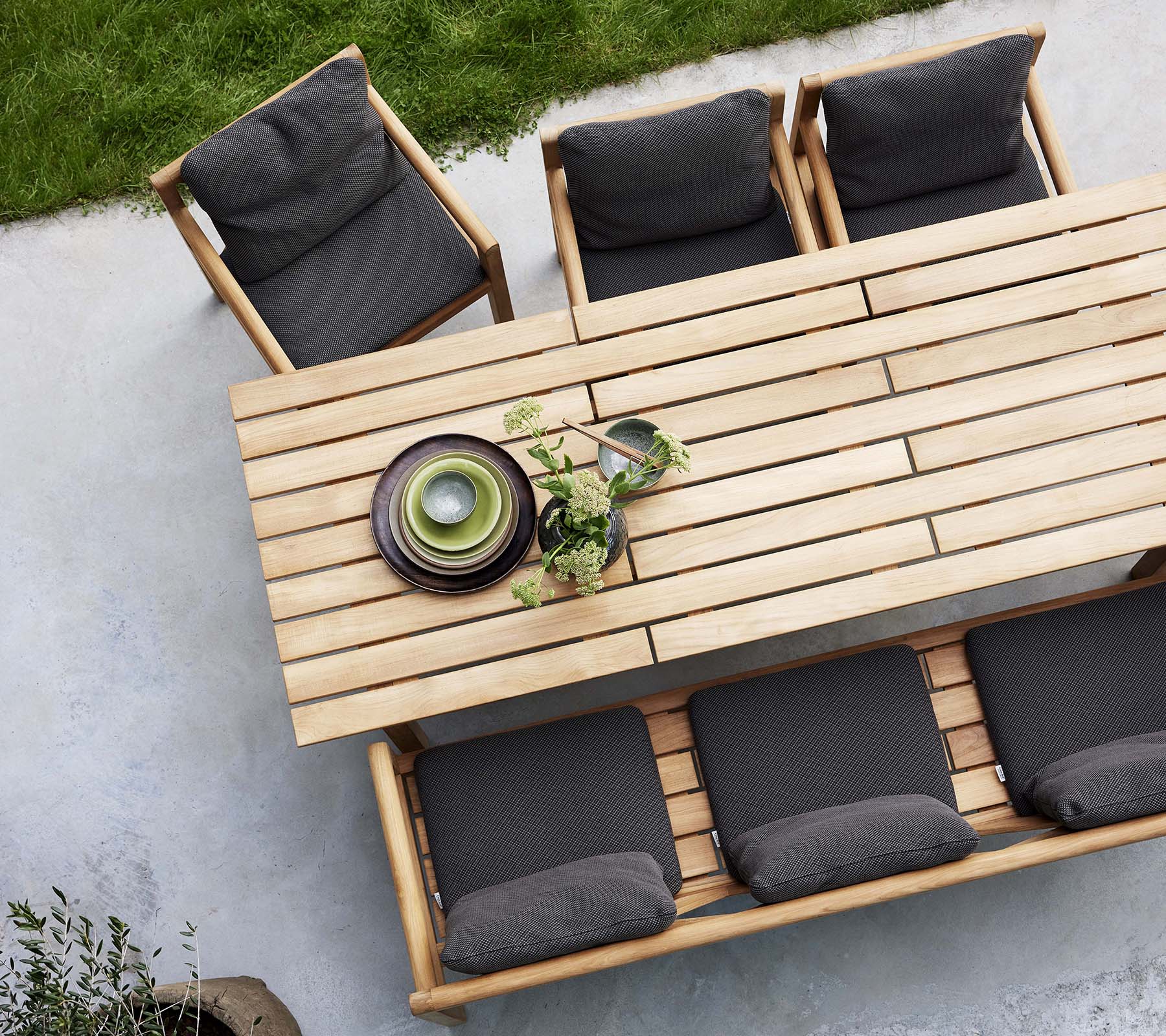 Een houten eetkamer set met een tafel, bank en stoelen met donkere kussens, geaccentueerd met decoratieve borden en groen.