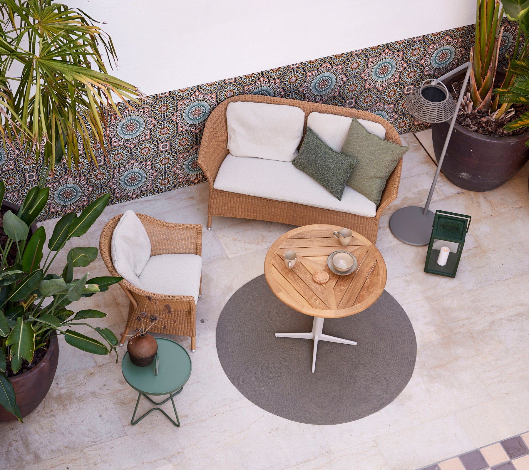 Een gezellige setting met een Lansing-sofa en stoel, een ronde tafel en groen, waardoor een ontspannen sfeer ontstaat. Perfect voor in je vrije tijd.