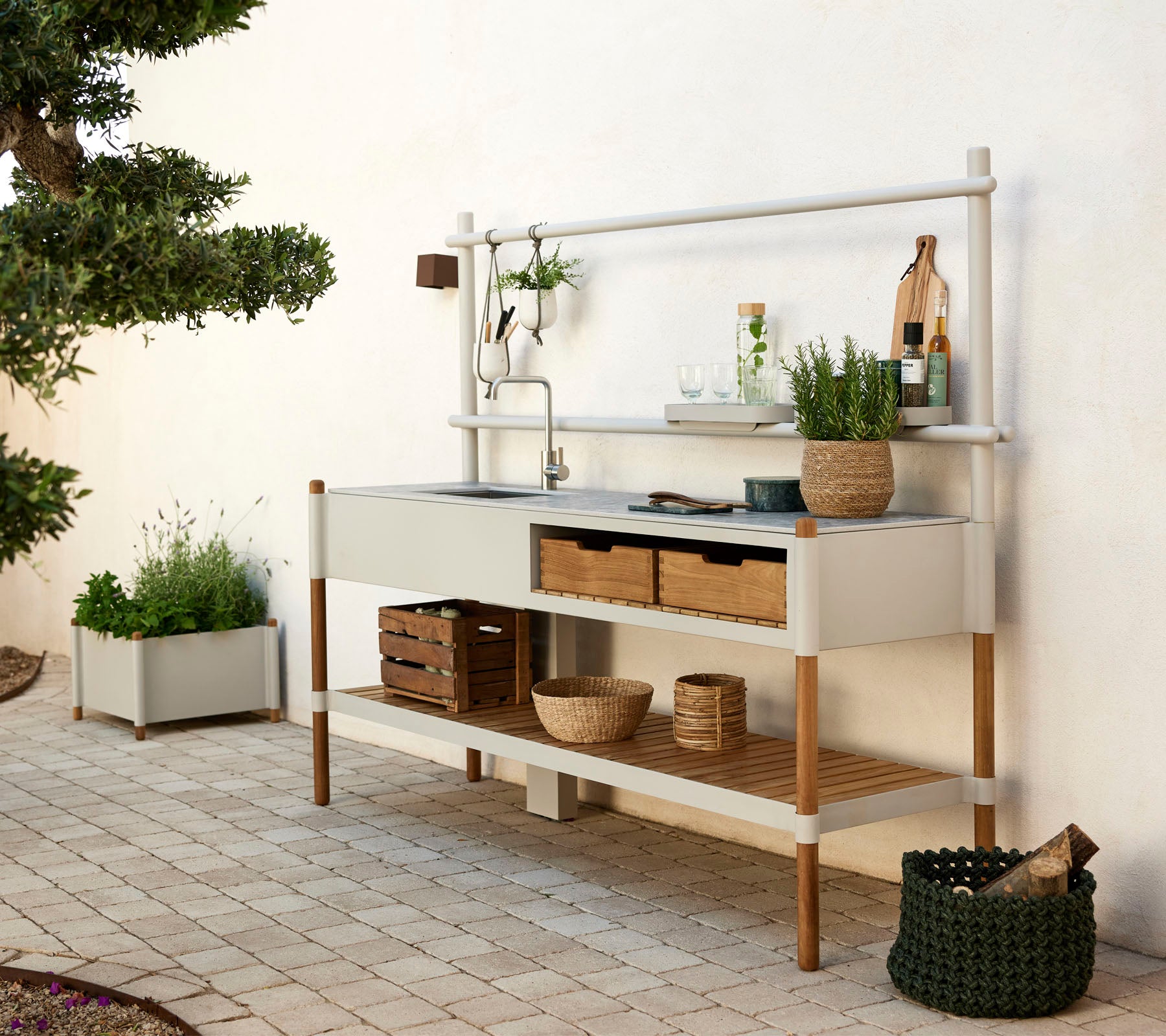 Moderne keukeneenheid met een metalen gootsteen, houten planken en decoratieve planten in stijlvolle containers. Eenvoudig ontwerp met natuurlijke elementen.