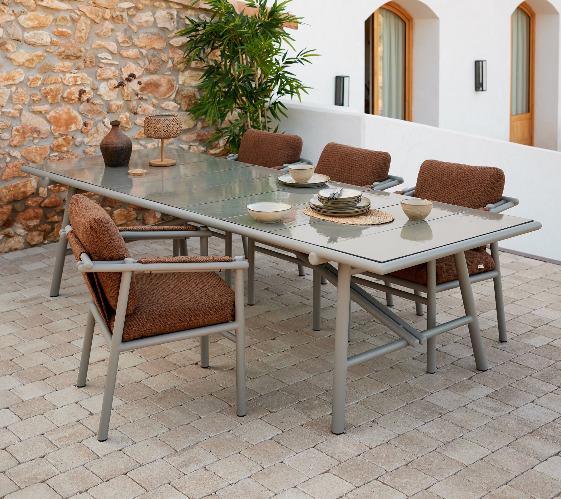 Een ruime eettafelset met aluminiumstangen, met bruin gevoerde stoelen en servies dat op een glazen oppervlak is gerangschikt.