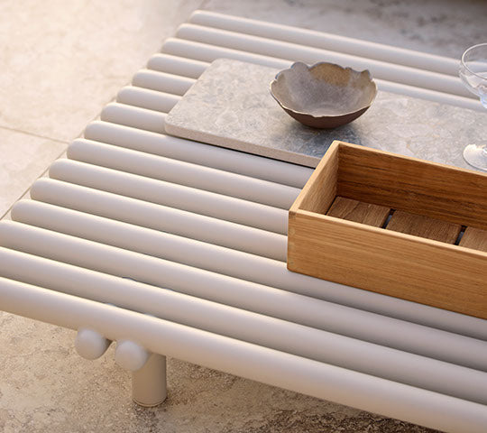 Aluminium salontafel met een lattenontwerp, met een houten opbergbox en een keramische kom op een minimalistisch oppervlak.