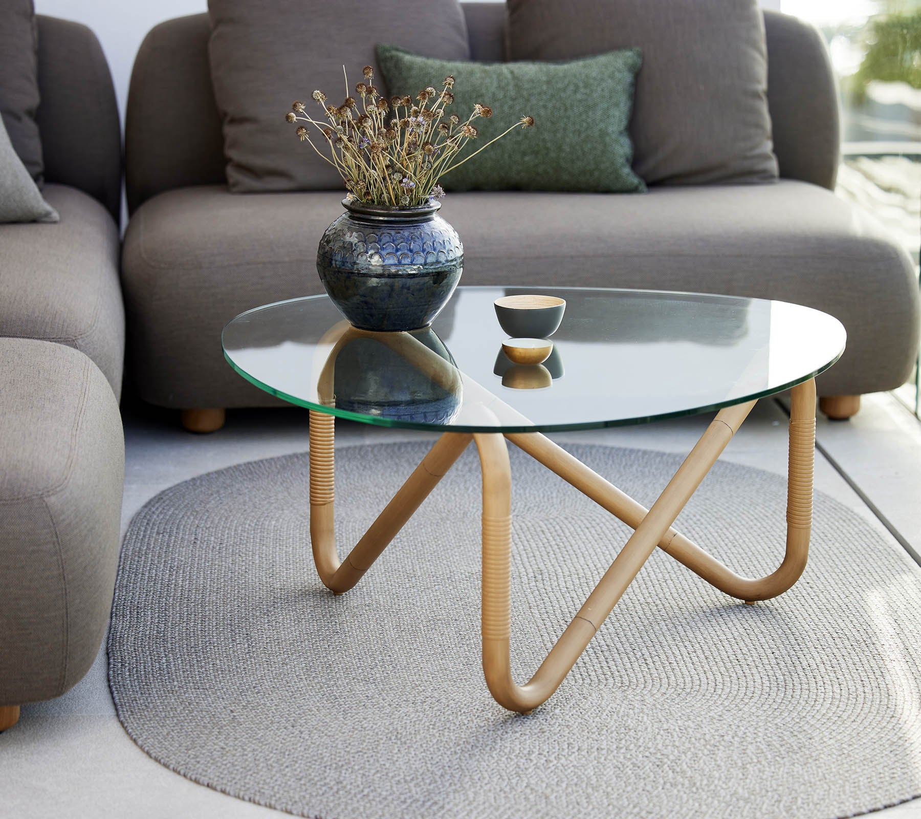 Golf koffie tafel met glazen blad en houten basis, geaccentueerd door een vaas en een kleine schaal, omringd door zachte, neutraal gekleurde zitplaatsen.