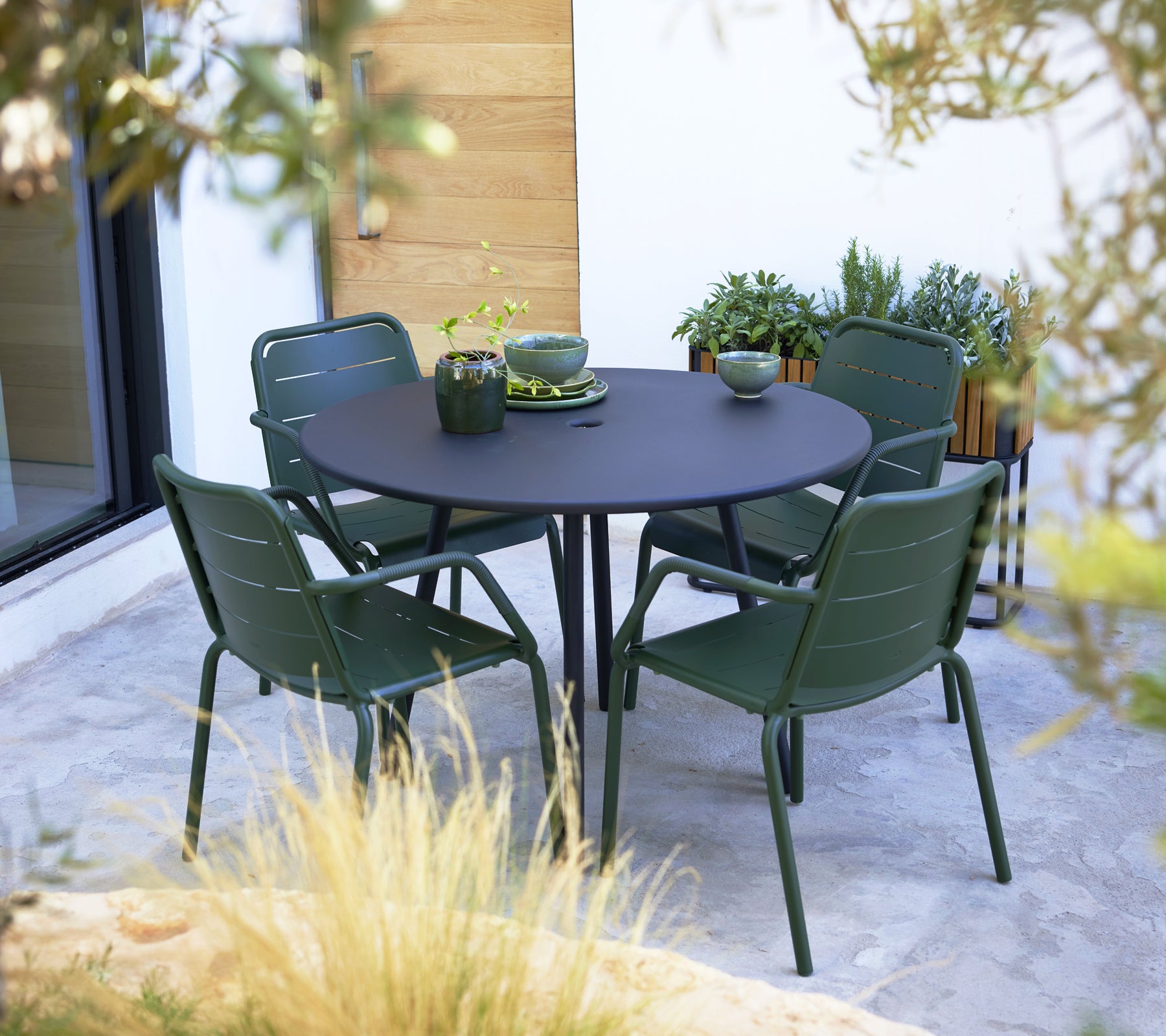 Groene Kopenhaagse fauteuils rond een ronde zwarte tafel, aangevuld met decoratieve schalen en planten op het oppervlak.