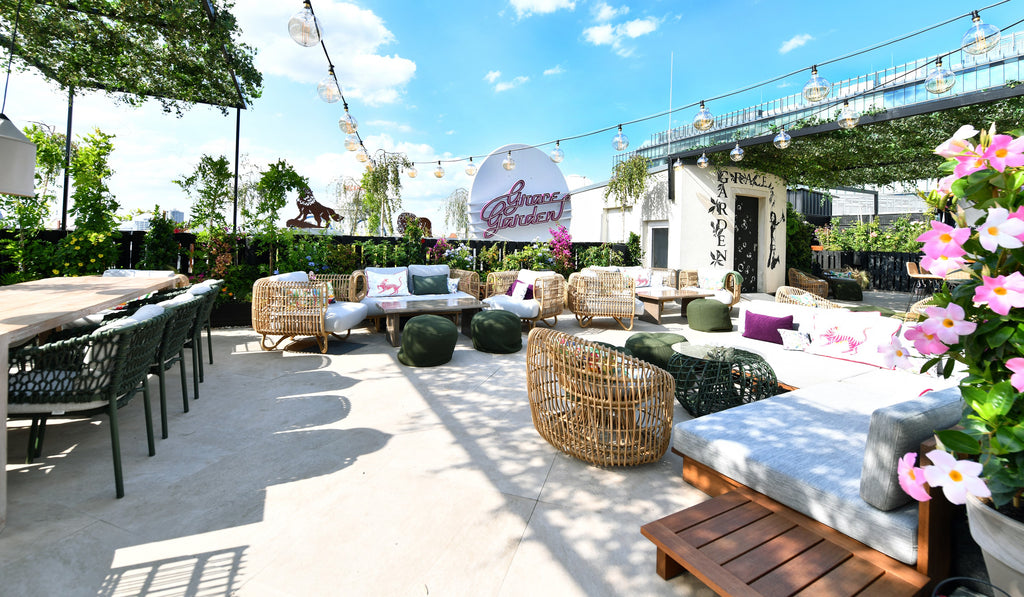 Grace Garden, roofttop bar and lounge in Berlin, blue sky, terrace furnished with dark green outdoor dining chairs, natural lounge chairs, round lounge chairs, green plants, flowers rosa
