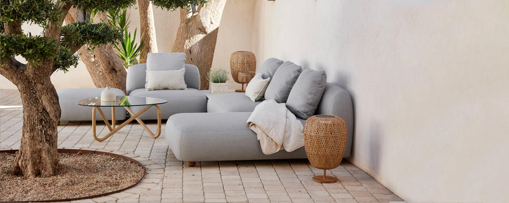Stijlvolle zitruimte met zachte grijze sofa's, decoratieve kussens, een gezellige plaid en natuurlijke elementen zoals een potplant en gevlochten bijzettafels.