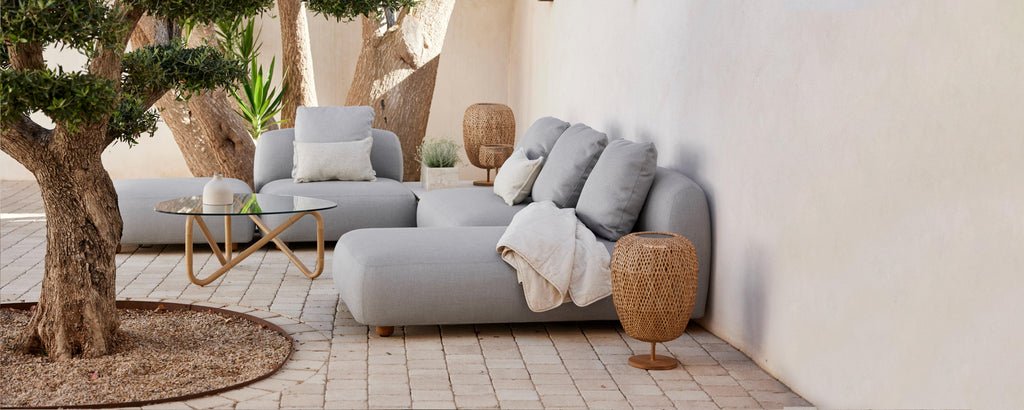 Stijlvolle zitruimte met zachte grijze sofa's, decoratieve kussens, een gezellige plaid en natuurlijke elementen zoals een potplant en gevlochten bijzettafels.