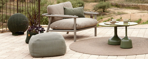 Stijlvol zitgedeelte met een comfortabele stoel, ronde tafel, pouf en decoratieve accessoires op een gestructureerd tapijt gerangschikt.