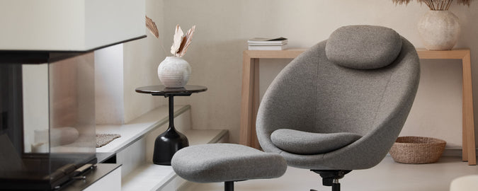 Gezellige grijze stoel met een bijpassende voetensteun naast een moderne tafel en decoratieve elementen, waardoor een stijlvolle en uitnodigende ruimte ontstaat.
