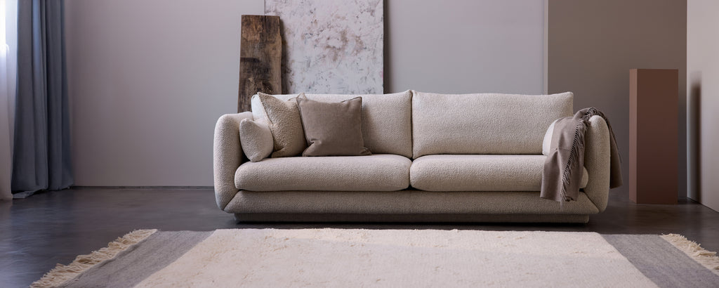 Moderne beige sofa met kussens en een grijze plaid in een minimalistische woonkamerinrichting.