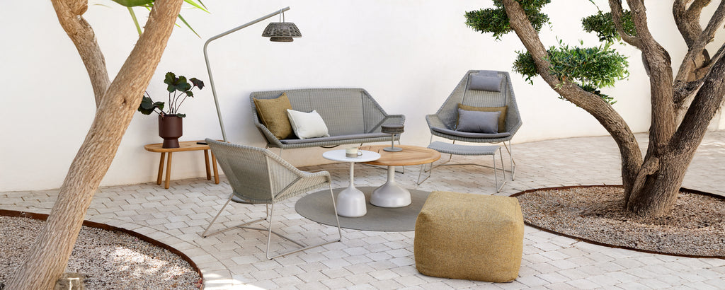 Moderne lounge-instelling met een grijze bank, een grijze stoel, een houten salontafel en een gele poef.
