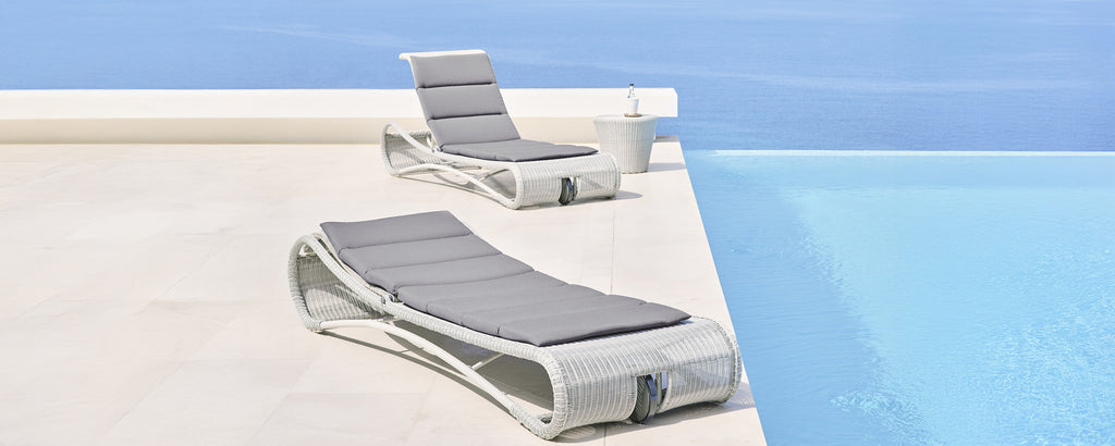 Moderne grijze en witte loungestoelen naast een zwembad.