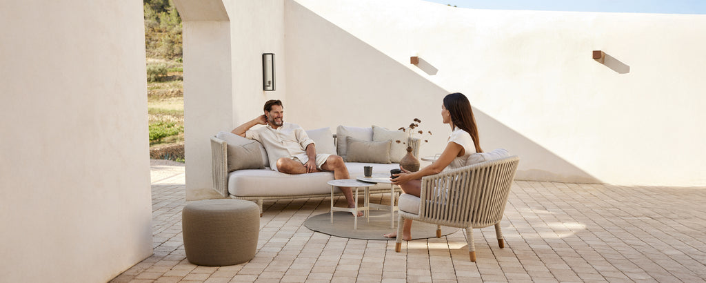 Moderne loungegebied met een beige bank, witte kussens, een grijze stoel en een ronde tafel.