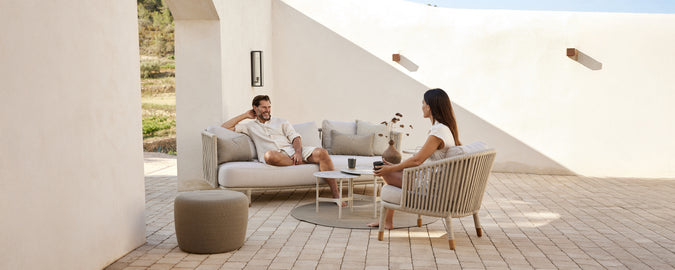 Moderne loungegebied met een beige bank, witte kussens, een grijze stoel en een ronde tafel.