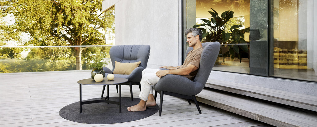 Modern loungegebied met grijze fauteuils, een zwarte tafel en een rond tapijt.