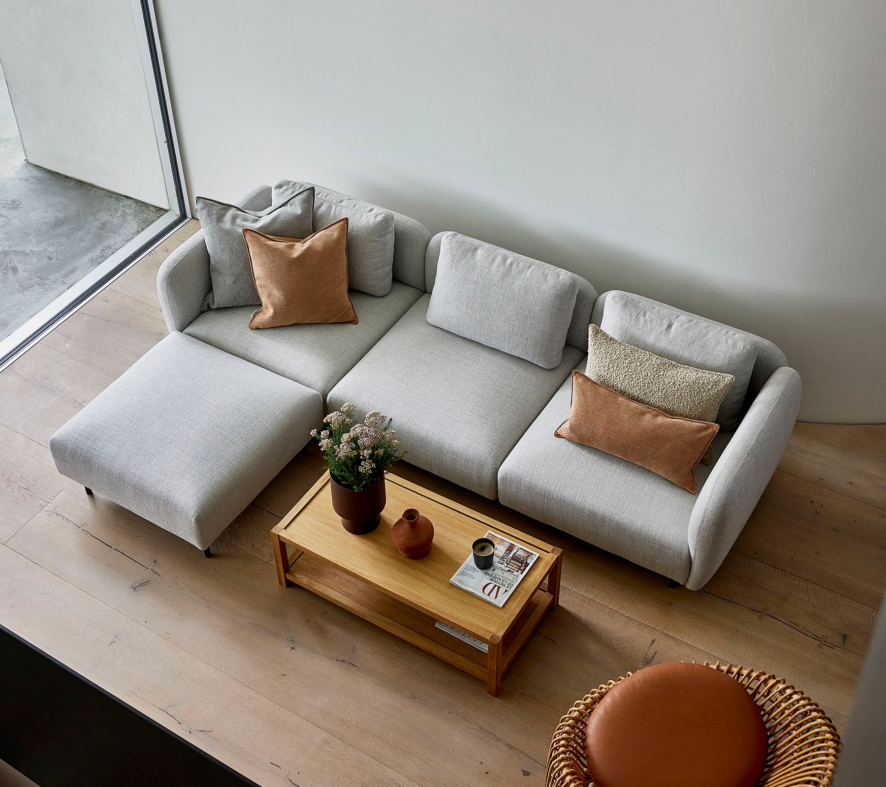 Een stijlvolle lichtgrijze hoekbank met kussens, gecombineerd met een houten salontafel en een ronde zitplek, die een gezellige sfeer creëert.