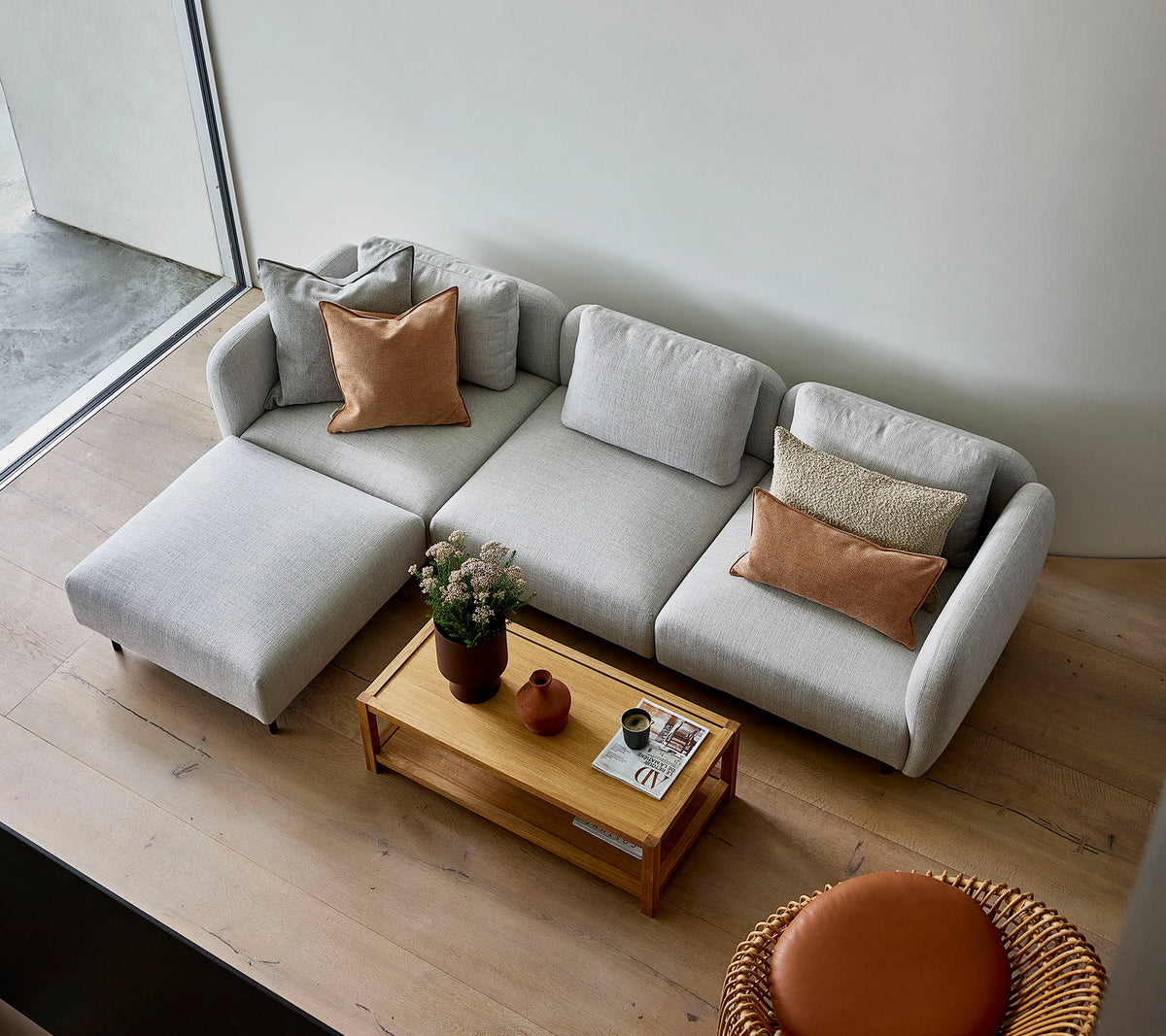 Een stijlvolle lichtgrijze hoekbank met kussens, gecombineerd met een houten salontafel en een ronde zitplek, die een gezellige sfeer creëert.