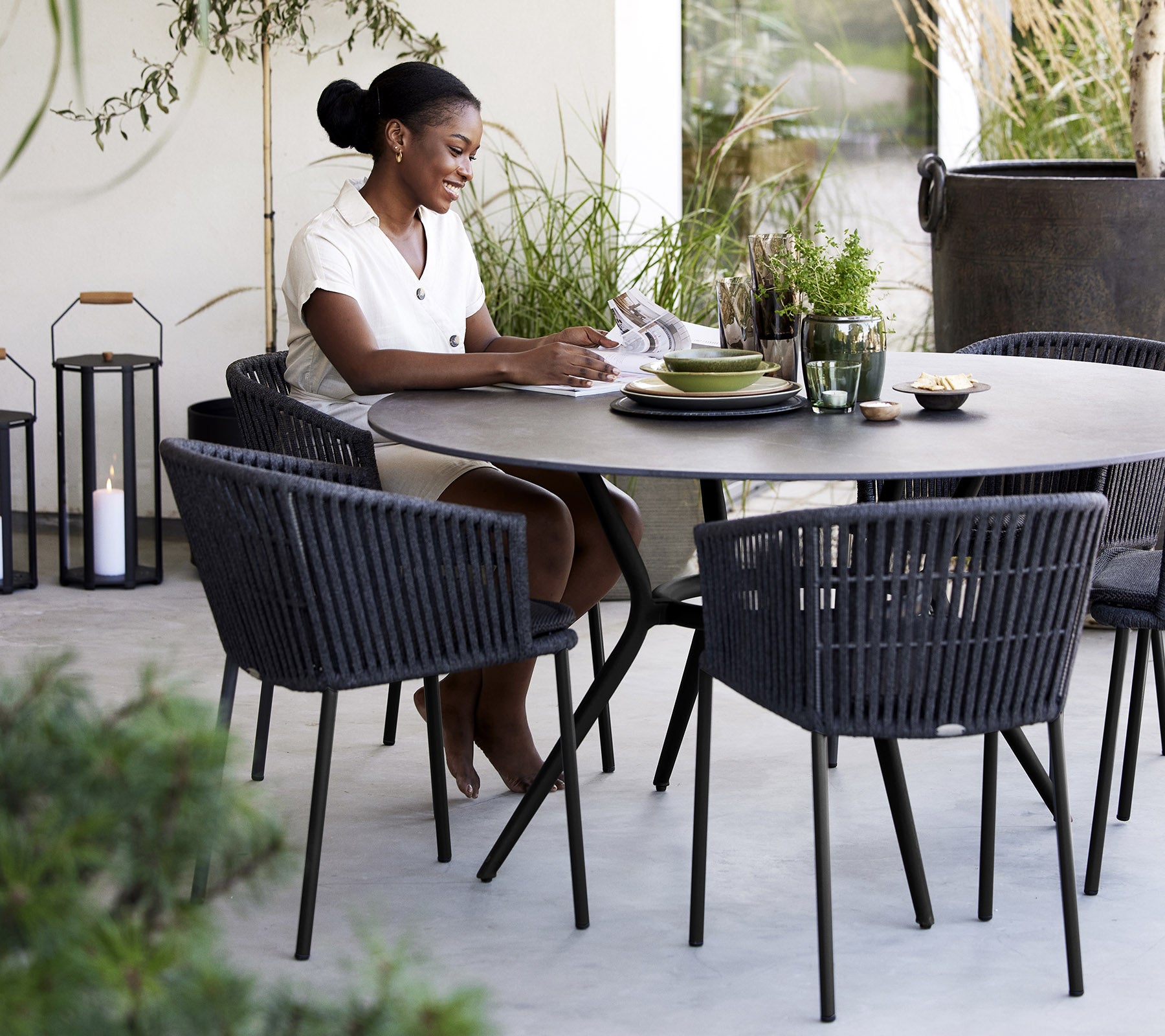 Een vrouw zit aan een ronde tafel en geniet van een maaltijd, omringd door stijlvolle stoelen en planten.