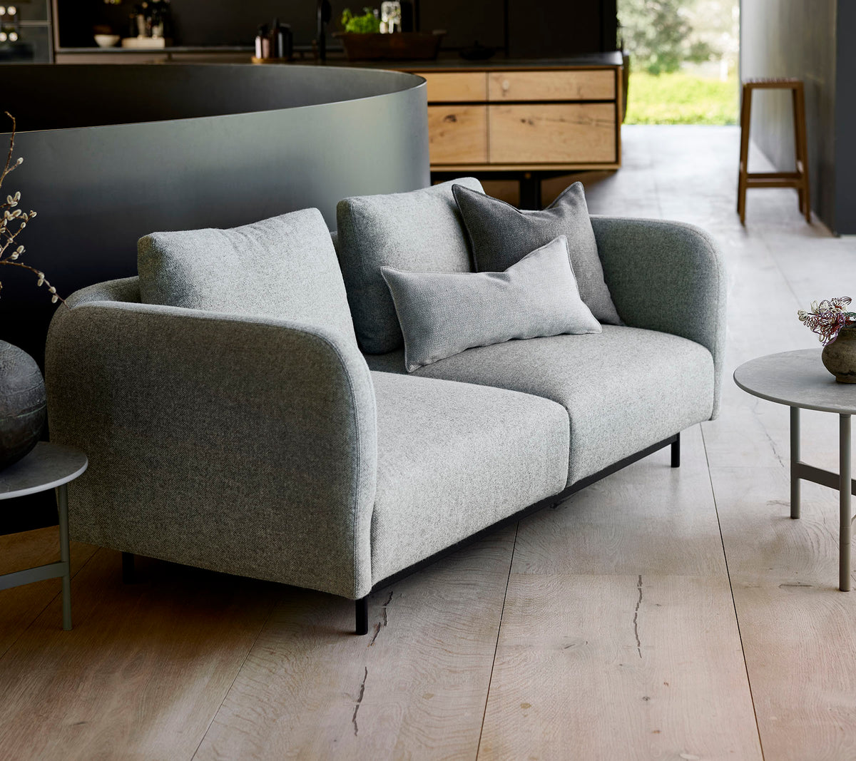 Moderne grijze bank met pluche kussens, gecombineerd met een kleine ronde tafel, tegen een minimalistisch achtergrond.