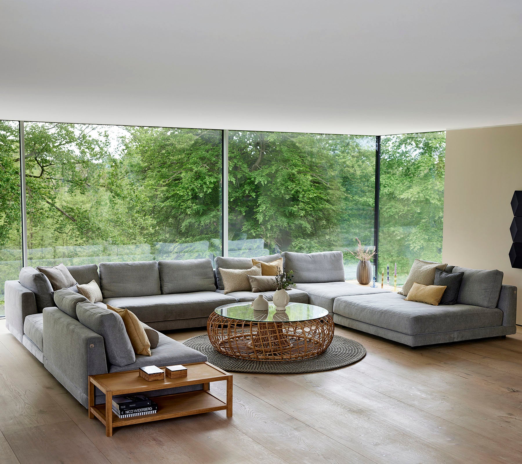 Ruime woonkamer met een grote hoekbank, salontafel en decoratieve accenten, omringd door natuurlijk licht en groen.