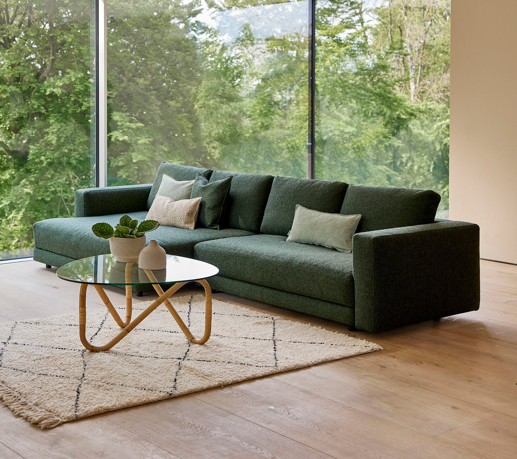Een moderne groene bank met kussens, vergezeld van een ronde salontafel en een decoratief tapijt, tegen een achtergrond van groen.