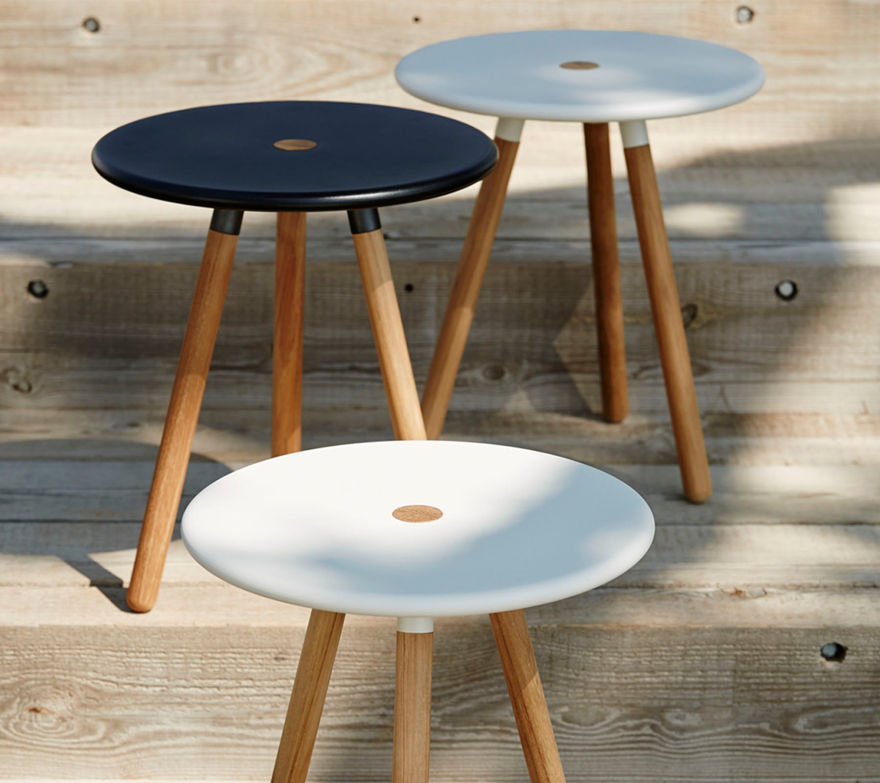 Drie minimalistische krukken met ronde zittingen in zwart en wit, elk ondersteund door houten poten, die een modern en stijlvol ontwerp uitstralen.