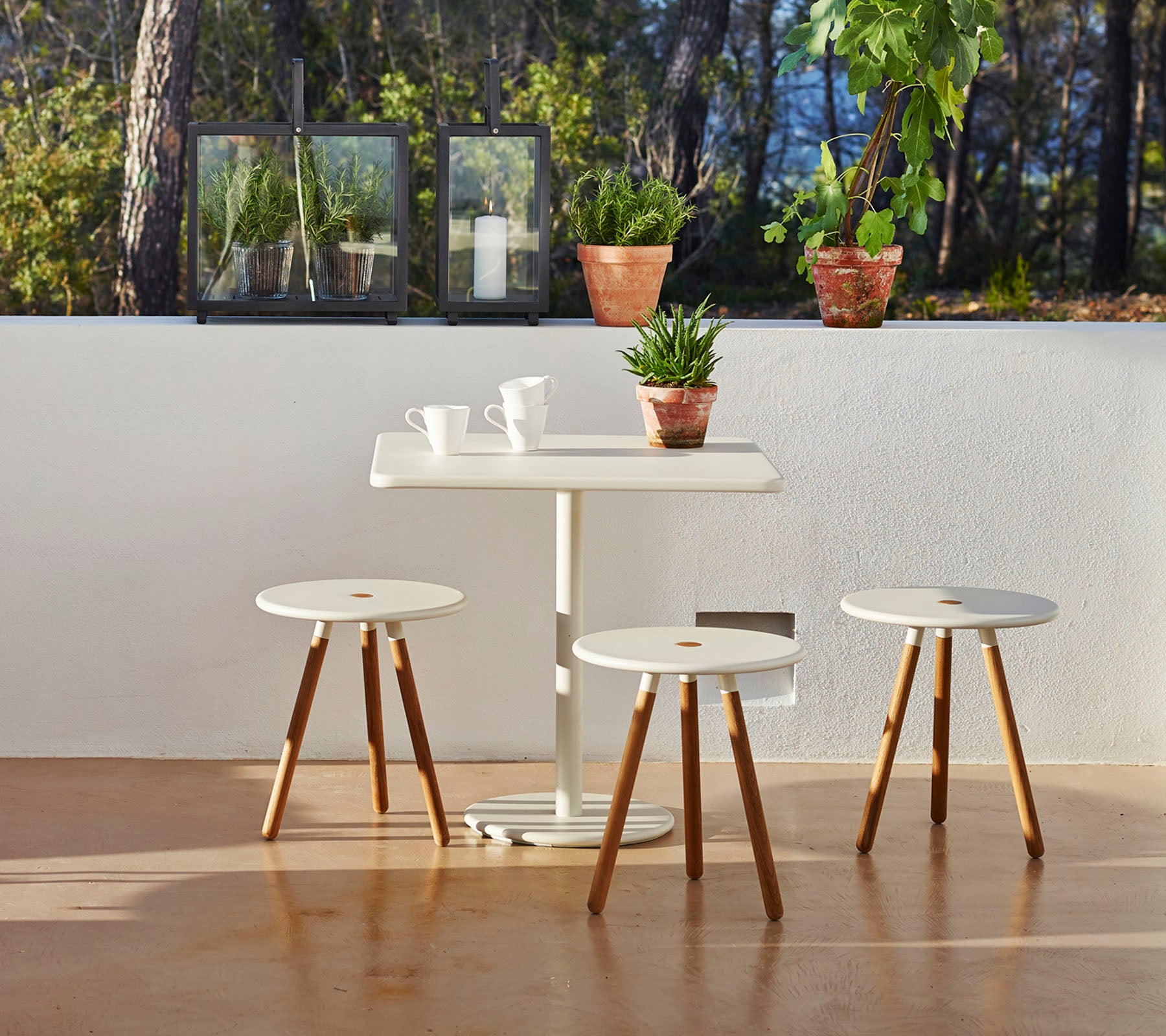 Een minimalistische tafel met drie bijpassende krukken, omringd door potplanten, die een serene en uitnodigende sfeer creëert.