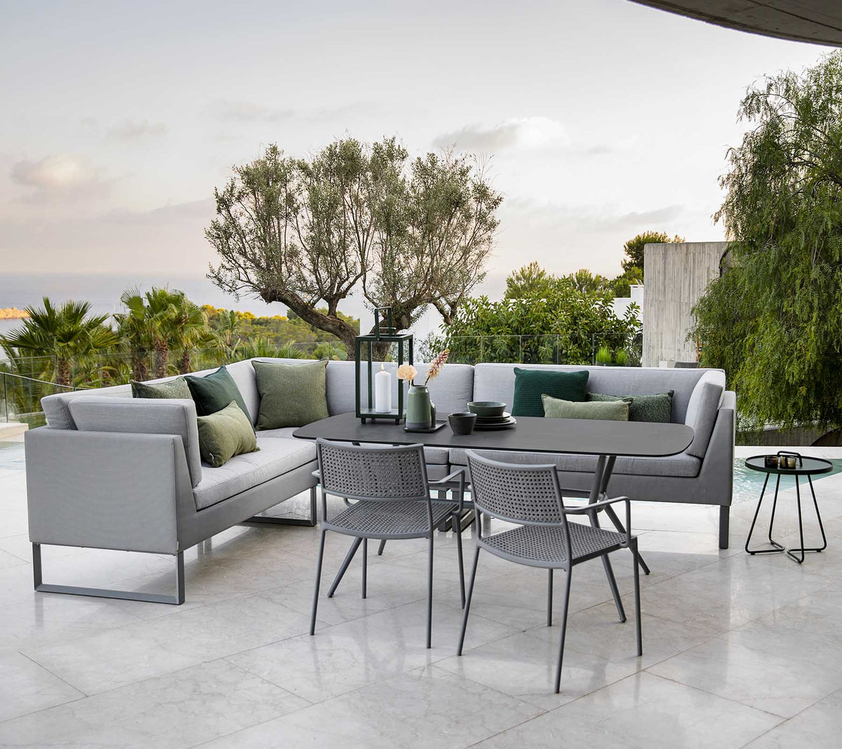 Moderne buitensitgebied met een stijlvolle loungebank, een eettafel en metalen stoelen omgeven door groen.