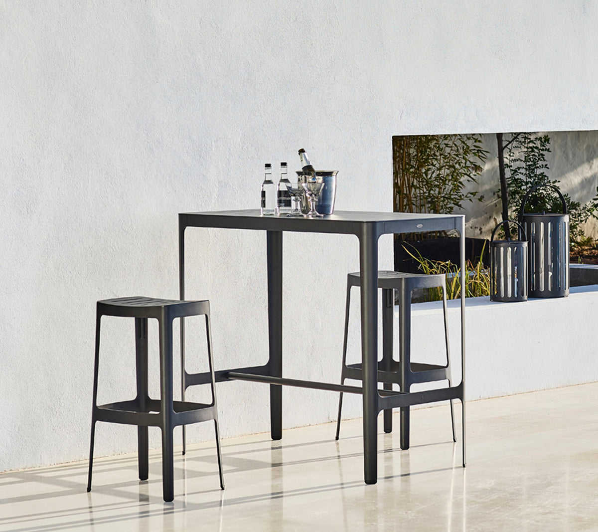 Een afgemaakte tafel met twee bijpassende krukken, met een minimalistisch ontwerp en flessen bovenop, tegen een neutrale achtergrond.