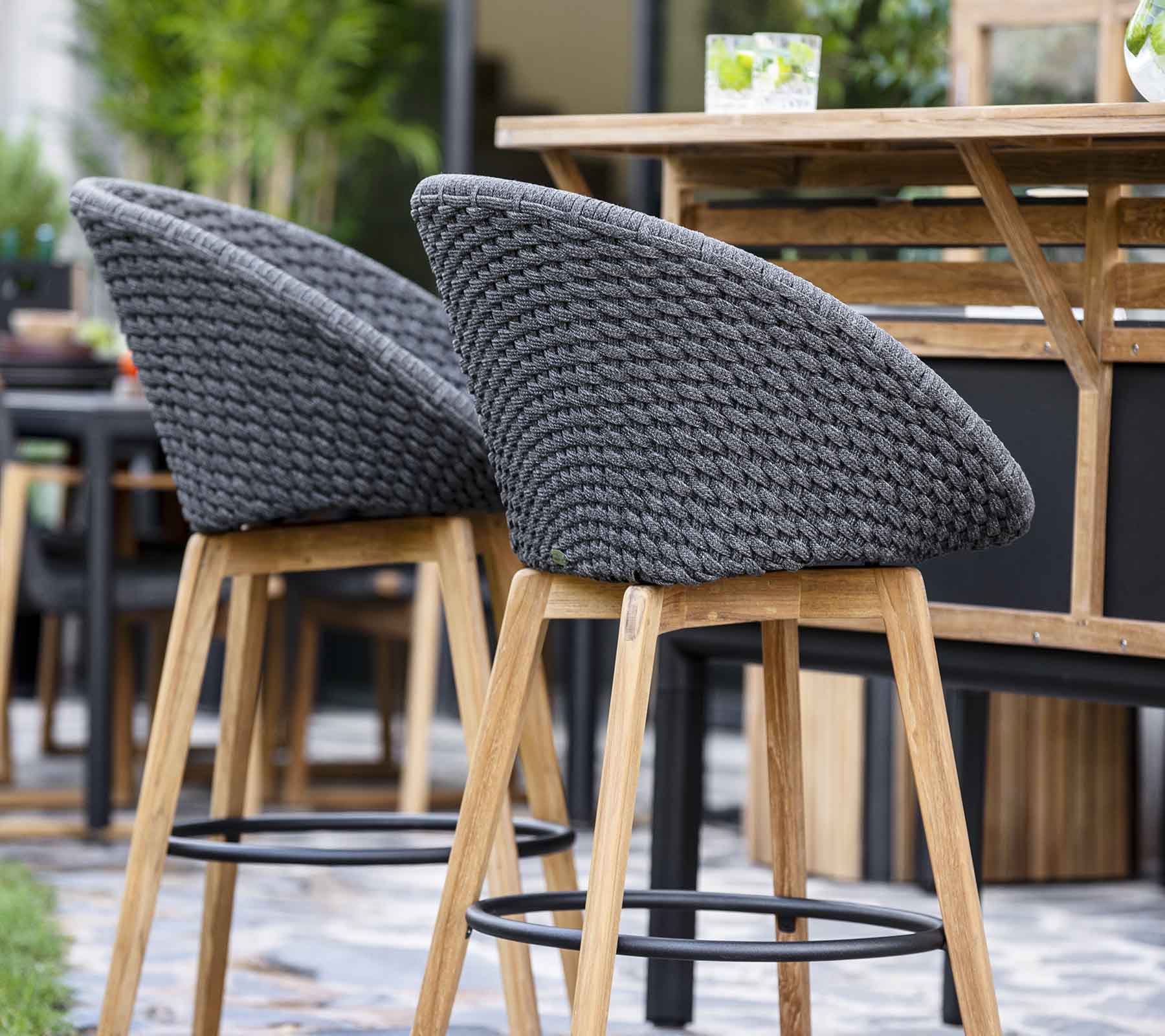 Stijlvolle barkrukken met geweven grijze ruggen en houten poten, geplaatst nabij een houten tafel in een eigentijdse setting.