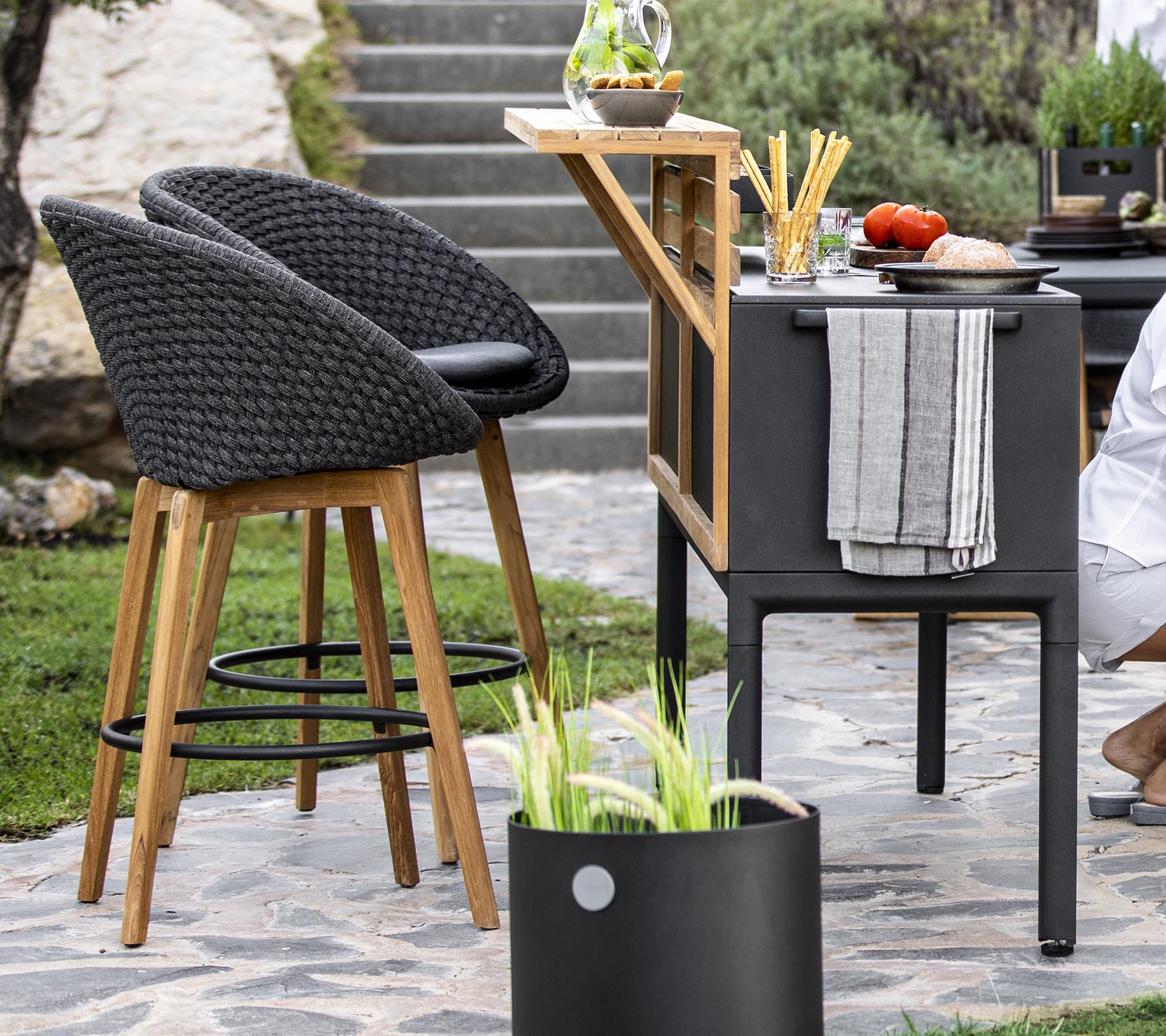 Stijlvolle buitenzitplaatsen met rotanstoelen, een moderne barkar en verse ingrediënten uitgestald op een werkblad, aangevuld met decoratieve planten.