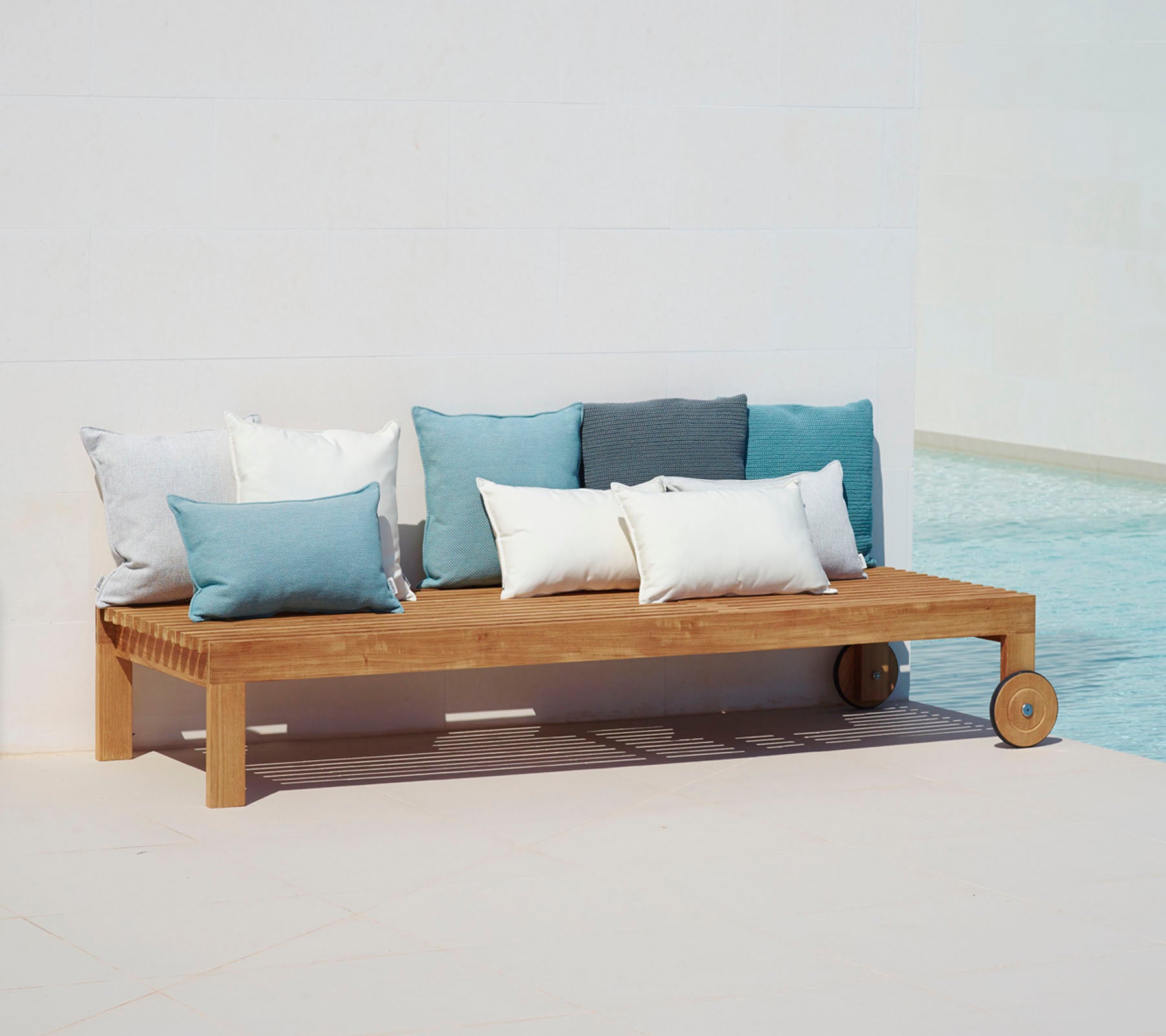 Houten loungesofa met een eenvoudig ontwerp, voorzien van kussens in blauw- en wittinten, geplaatst naast een zwembad.