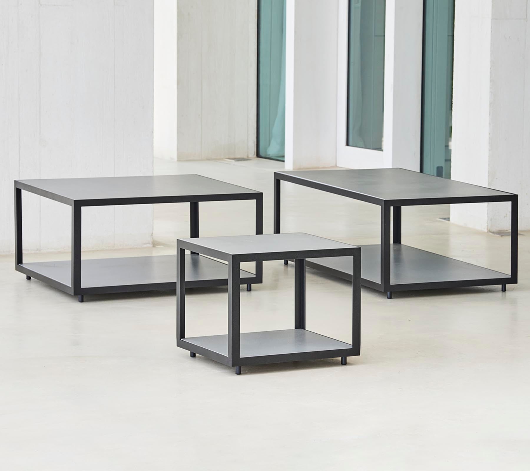 Drie moderne tafels met een minimalistisch ontwerp, met een slank frame en meerdere niveaus voor opslag of presentatie.