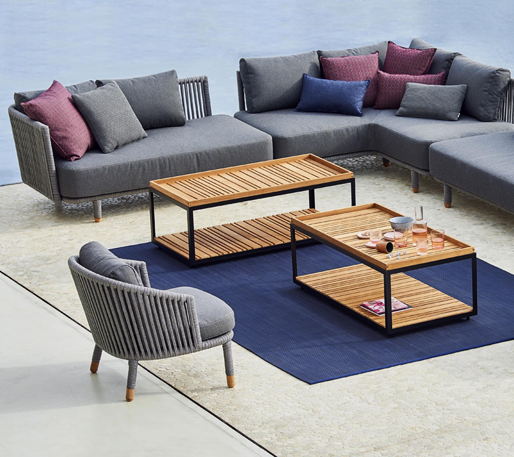 Moderne zitopstelling met een grijze hoekbank, een stijlvolle ronde stoel en houten salontafels met een blauw tapijt eronder.