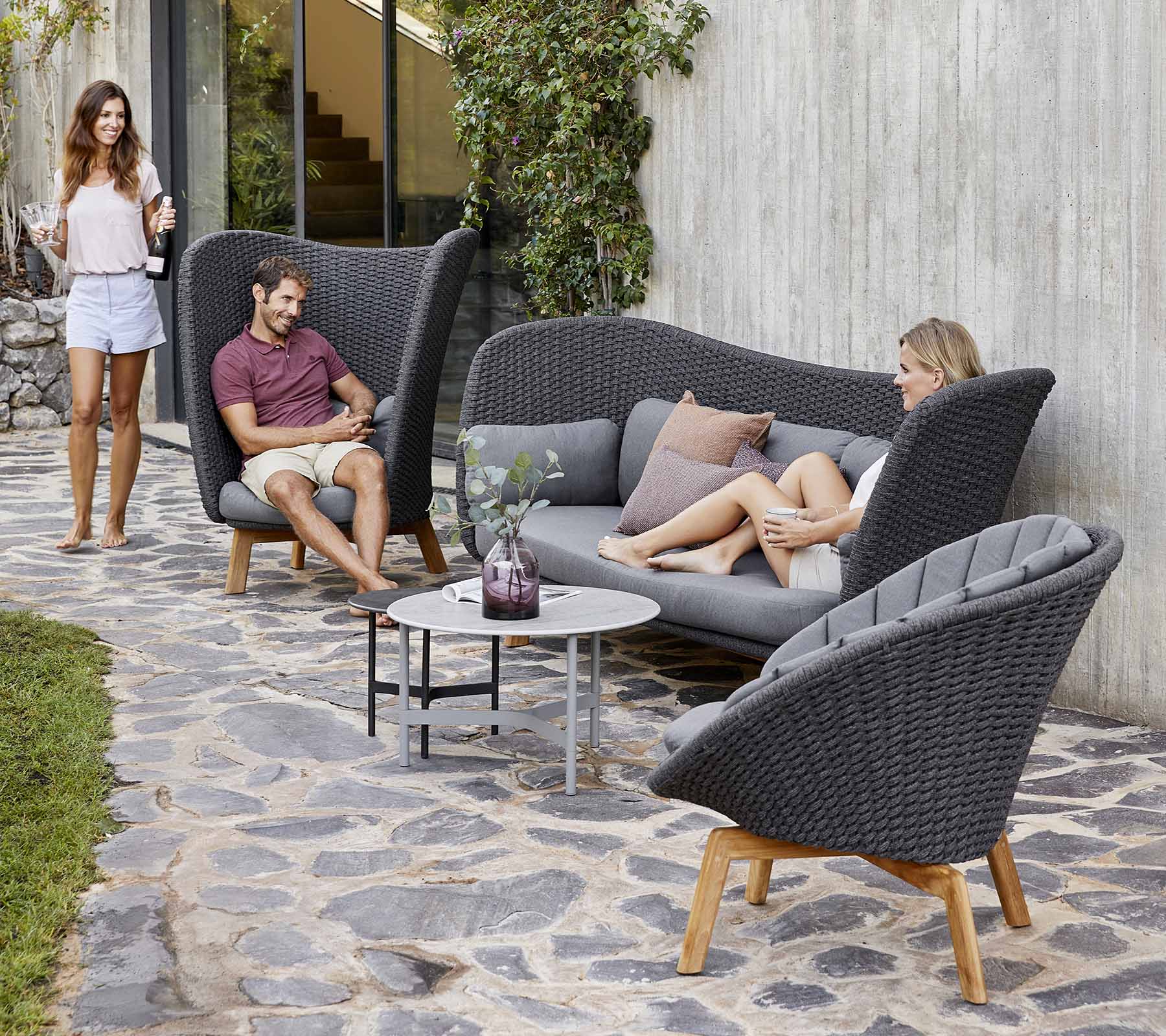Stijlvolle buitenzitarrangement met een gebogen bank en stoelen, met een kleine tafel, omringd door groen.