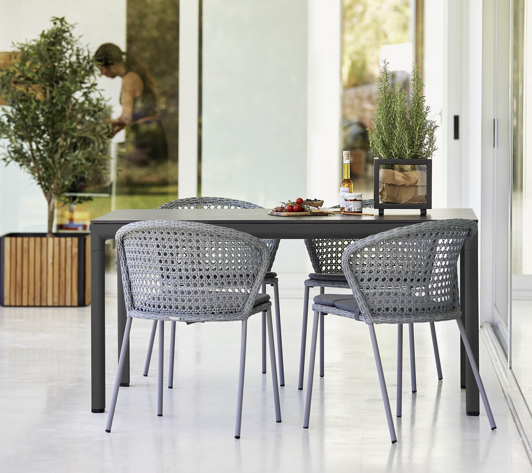 Moderne tafelaankleding met vier grijze gevlochten stoelen, versierd met kleine planten en een decoratief middelpunt. Heldere en uitnodigende sfeer.