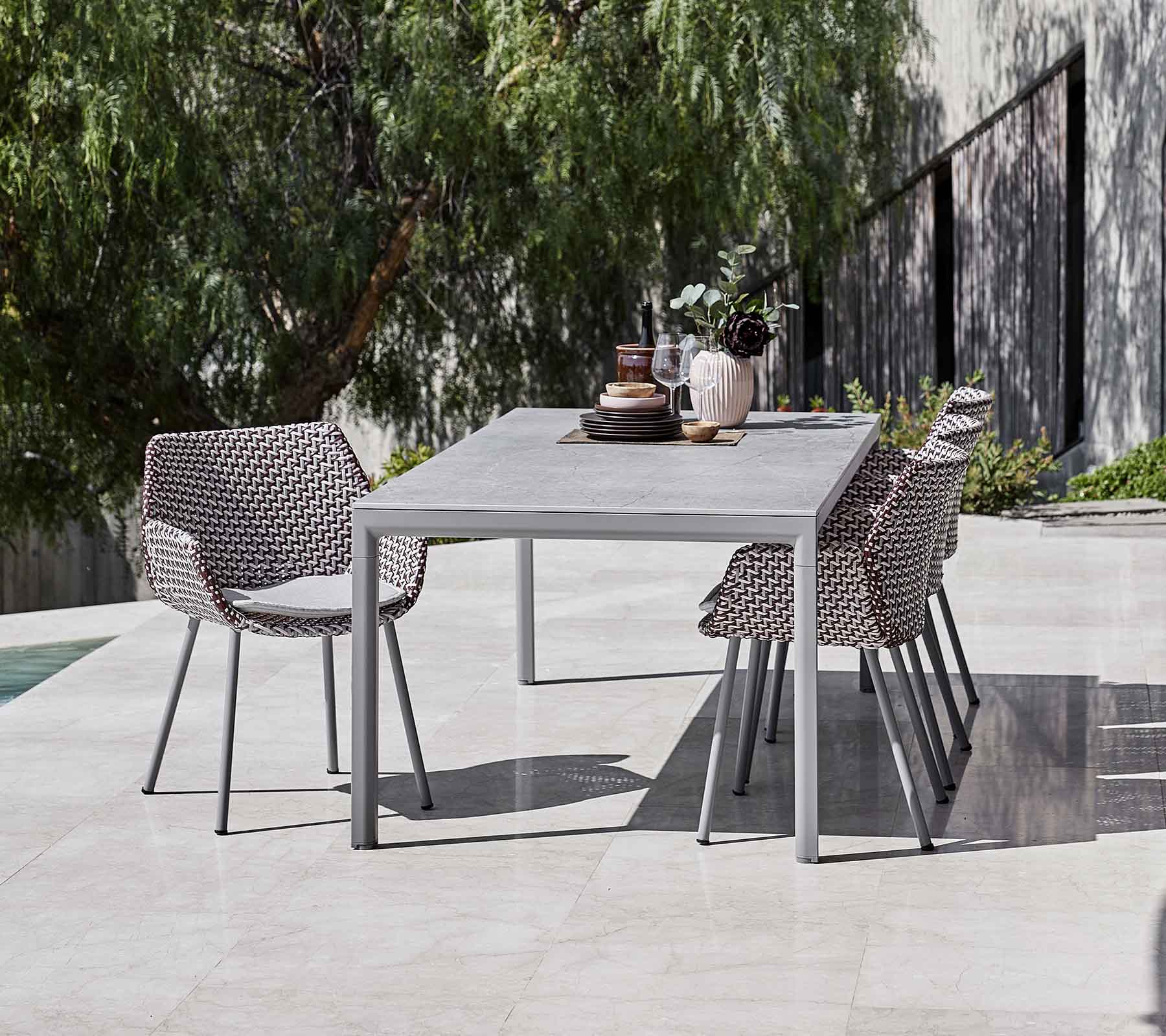 Een moderne eettafel omringd door stijlvolle, geweven stoelen, aangevuld met decoratieve vazen en groen in de achtergrond.